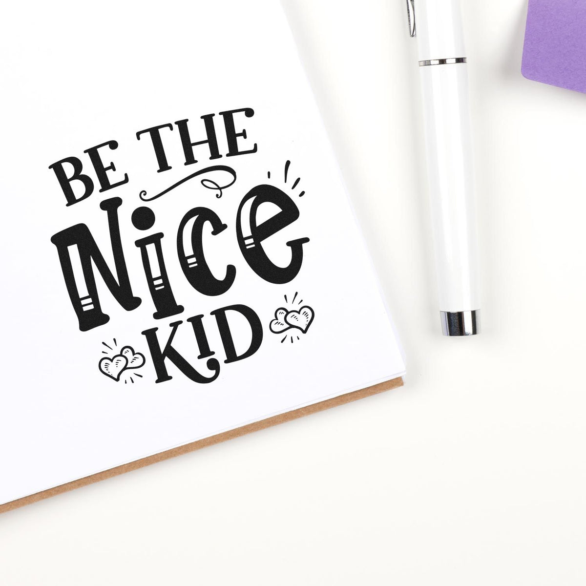 Black Be the Nice Kid stamp design on white card beside a white seal pen and purple stationery accents.