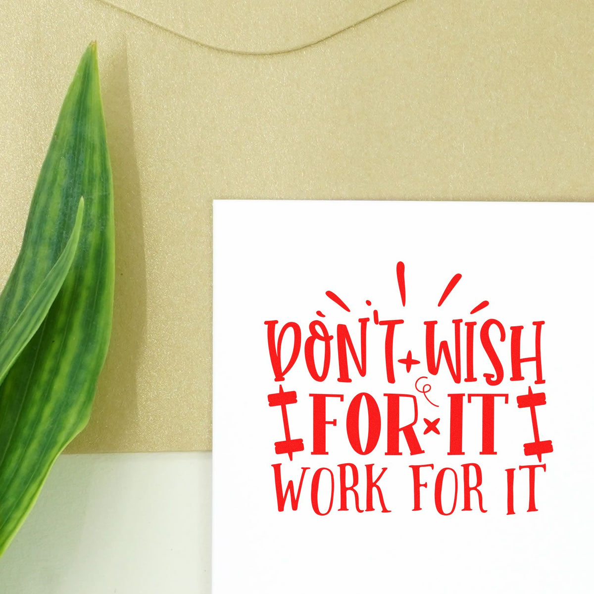 Red stamp seal with Dont Wish for It, Work for It in bold red on a white card, set against a gold background with a green leaf.