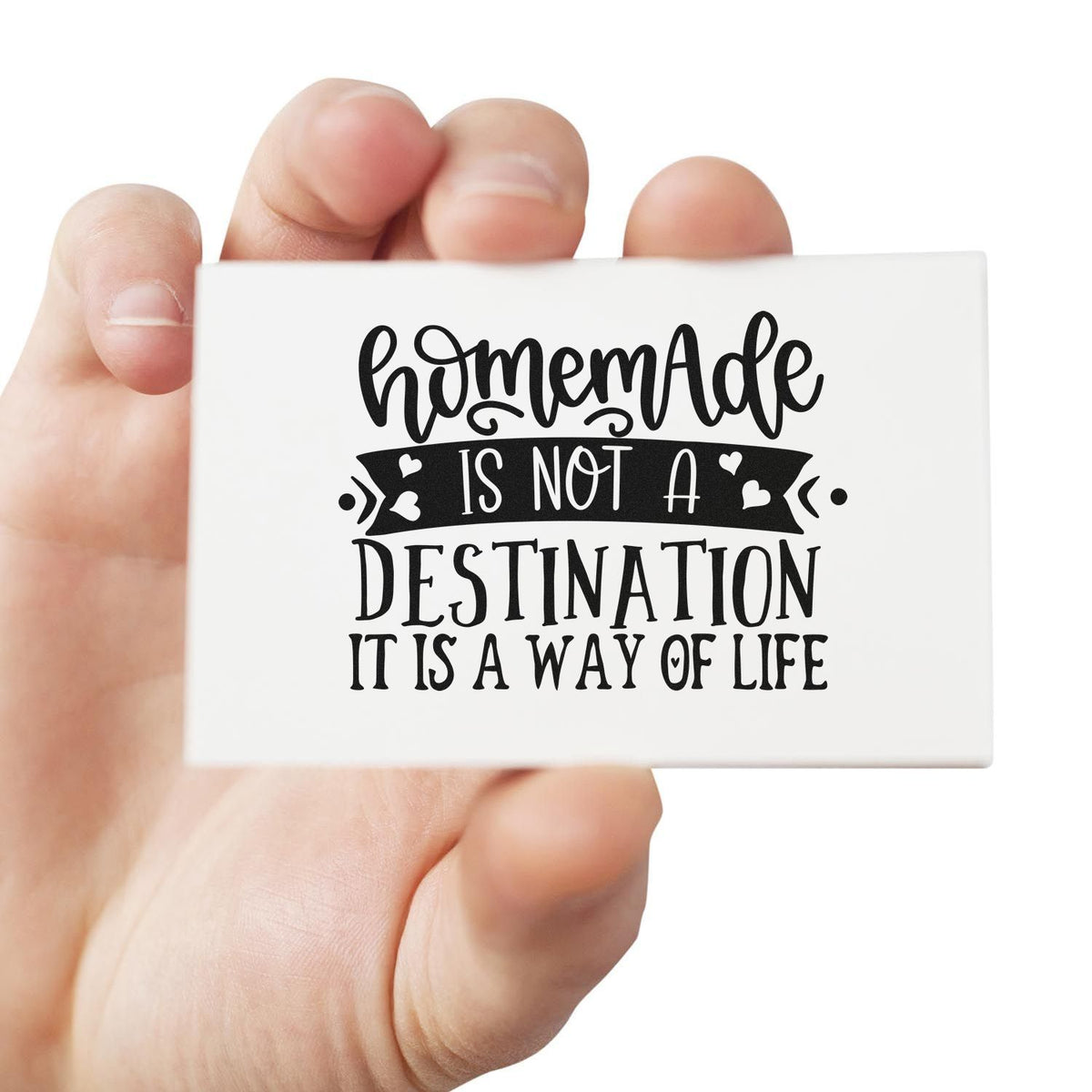 Handheld white rubber stamp seal with black handmade quote, hearts, and ribbon design: Homemade is not a destination