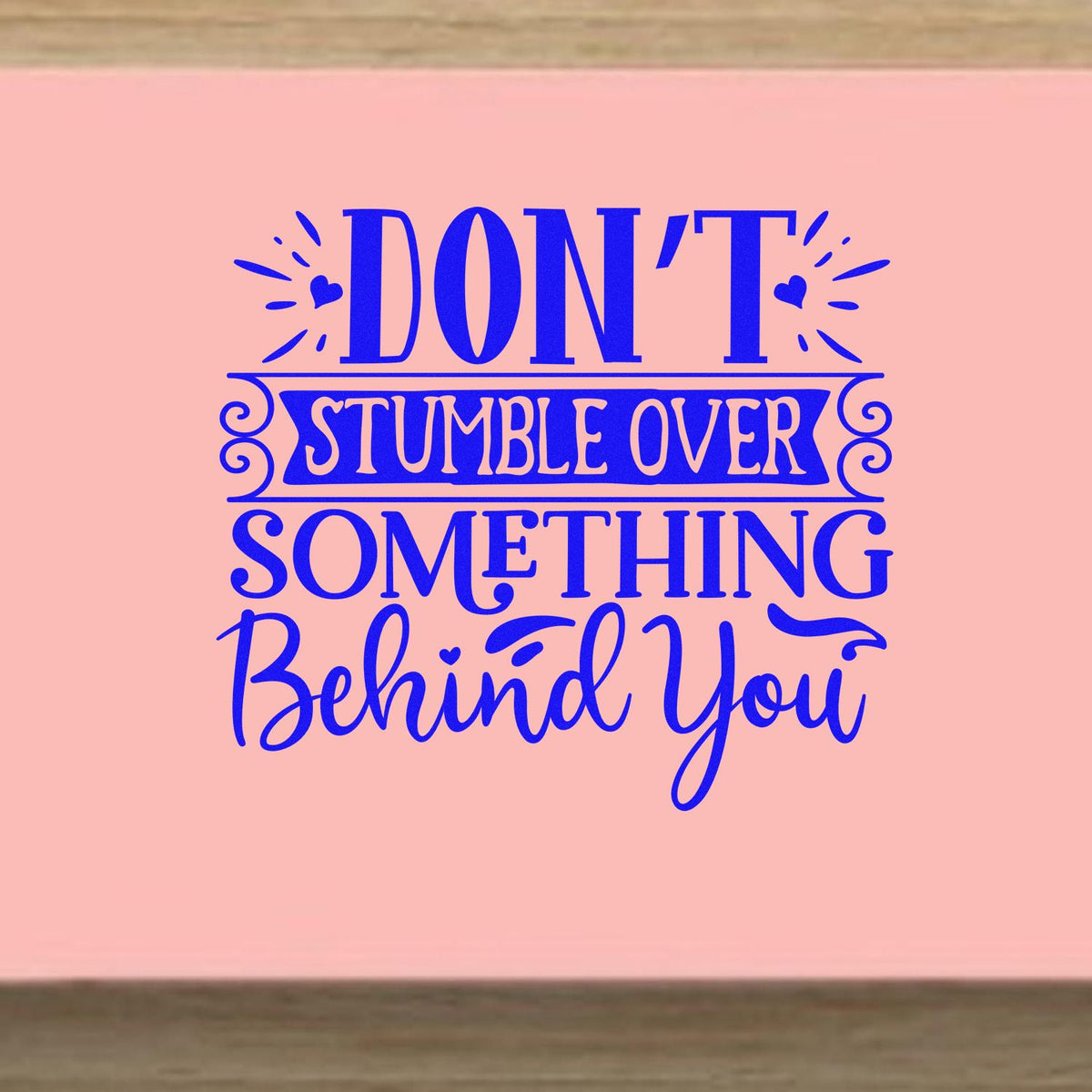 Pink decorative stamp/seal design with blue text, Dont stumble over something behind you, plus hearts and swirls.