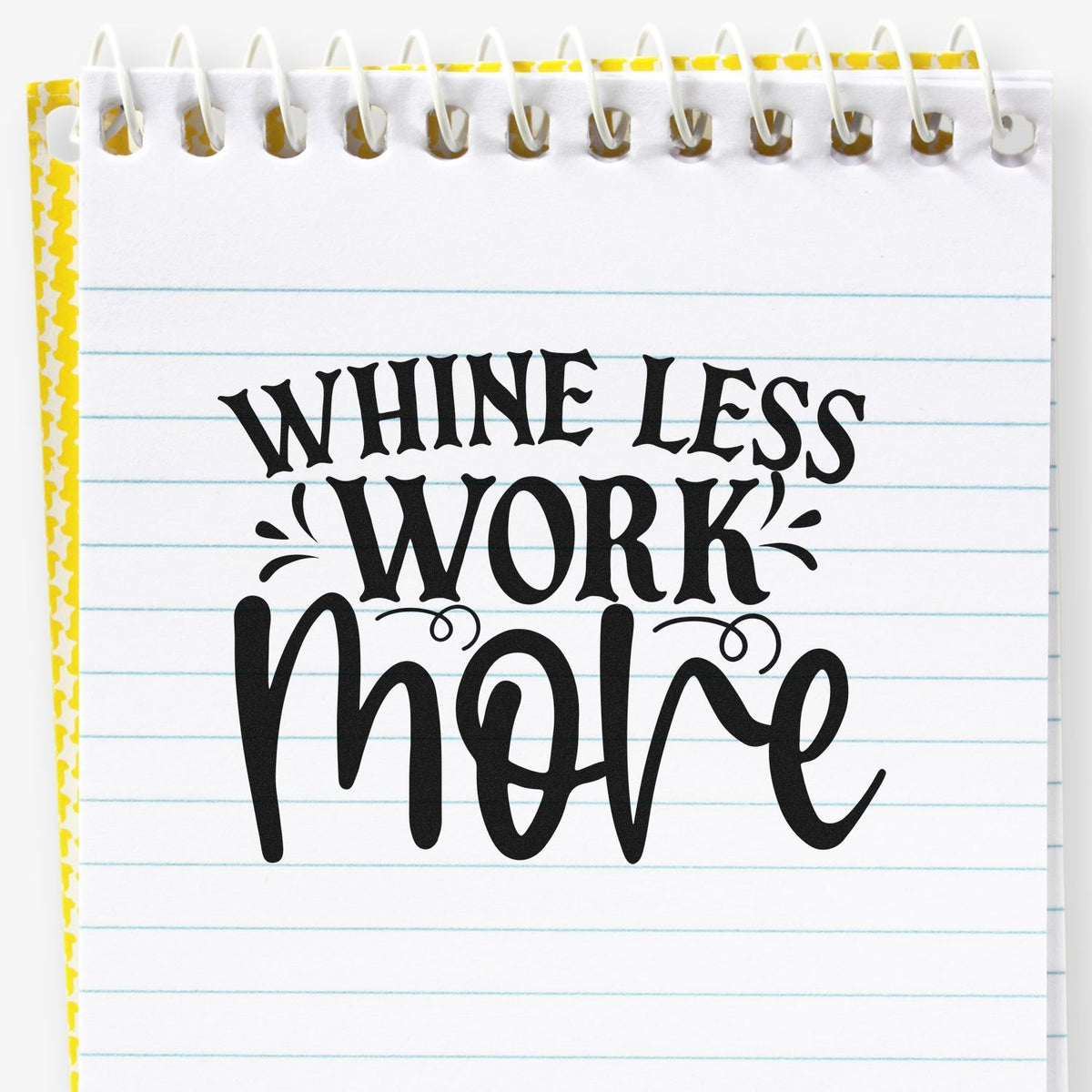 Black Whine Less Work More rubber stamp on white spiral notebook page with blue lines and yellow patterned edge seal.