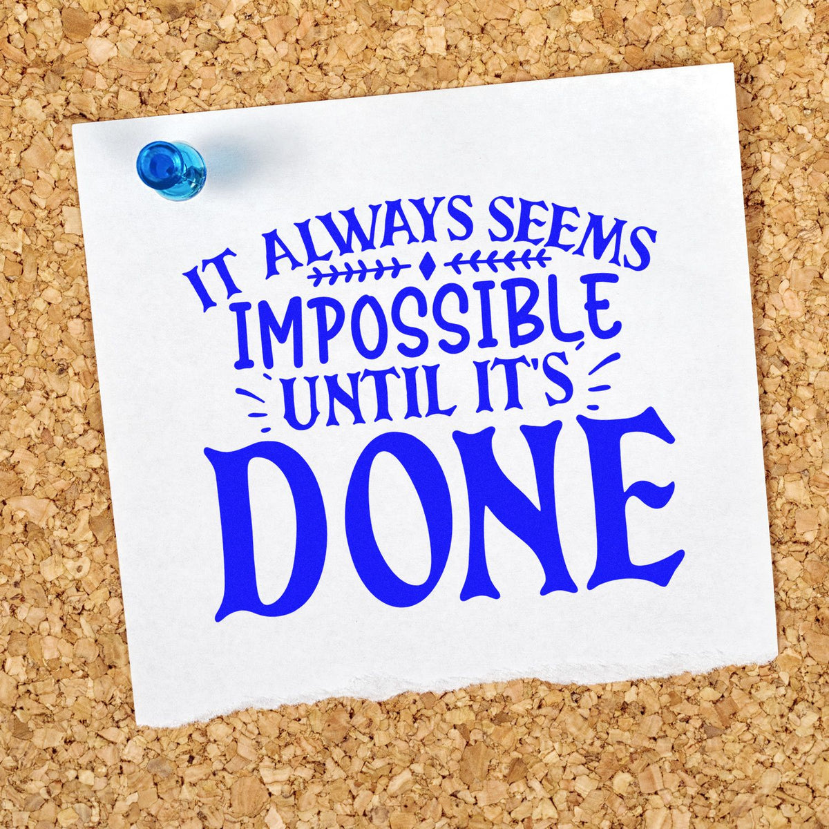 Blue rubber stamp and seal quote on white paper pinned to corkboard: It always seems impossible until its done.