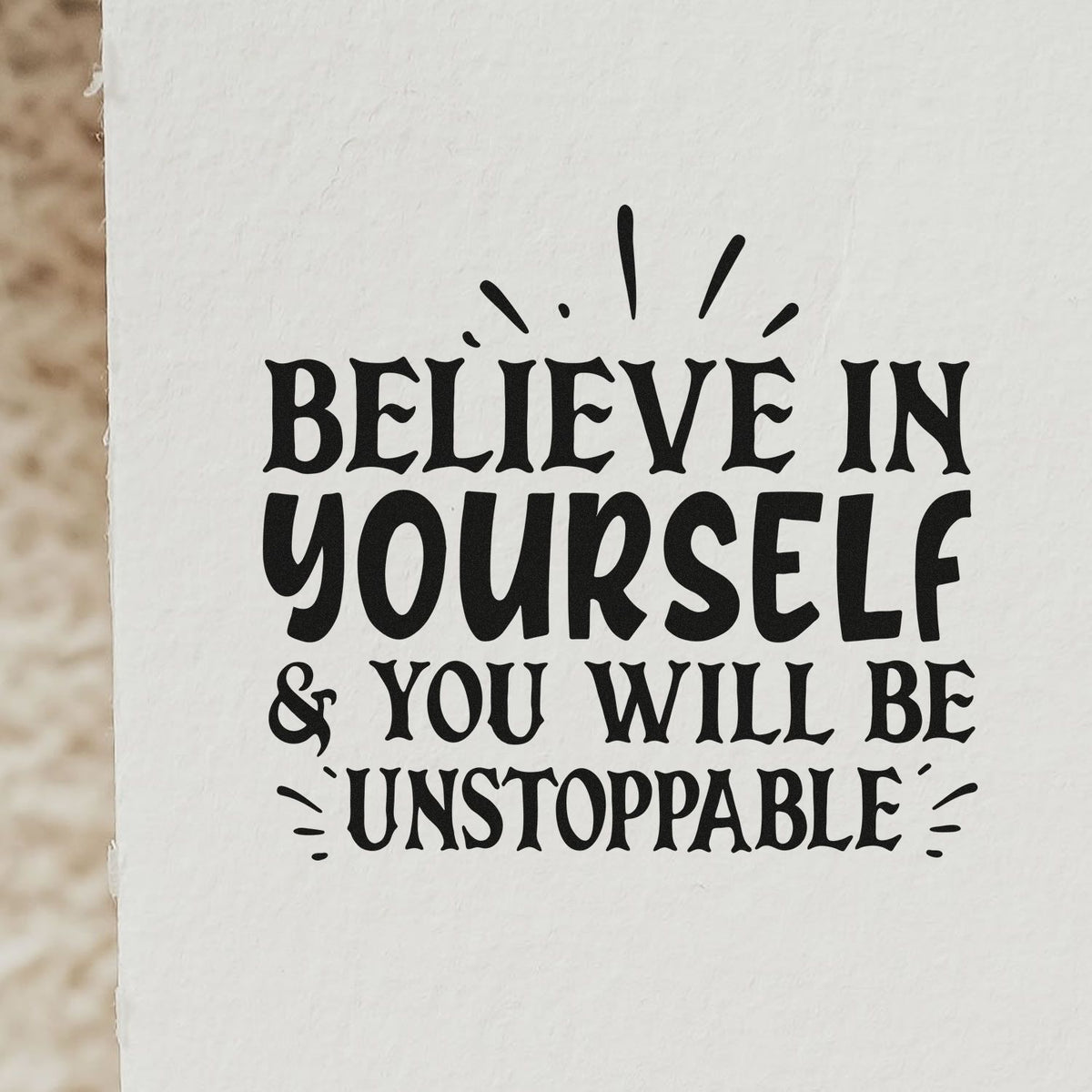 Black stamp seal with bold black text, Believe in yourself & you will be unstoppable, on white paper.