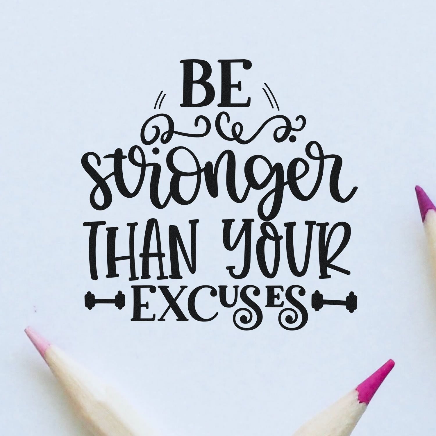 Black decorative stamp and seal reading Be stronger than your excuses on white paper, with pink pencil tips.