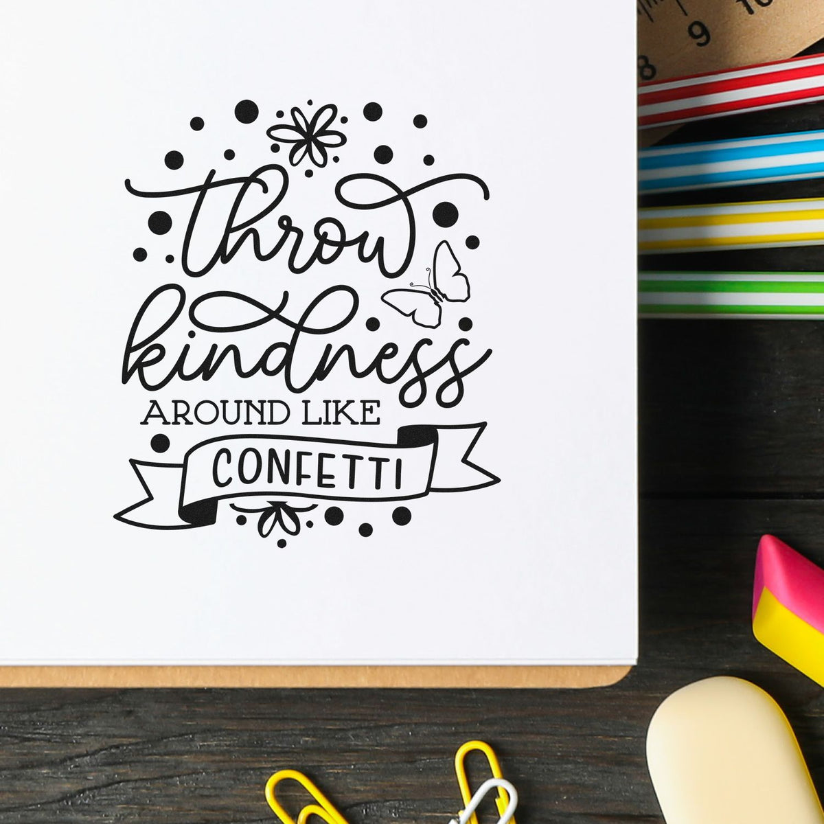 Black decorative stamp reading Throw kindness around like confetti with butterfly accents beside colorful seal ink pads.
