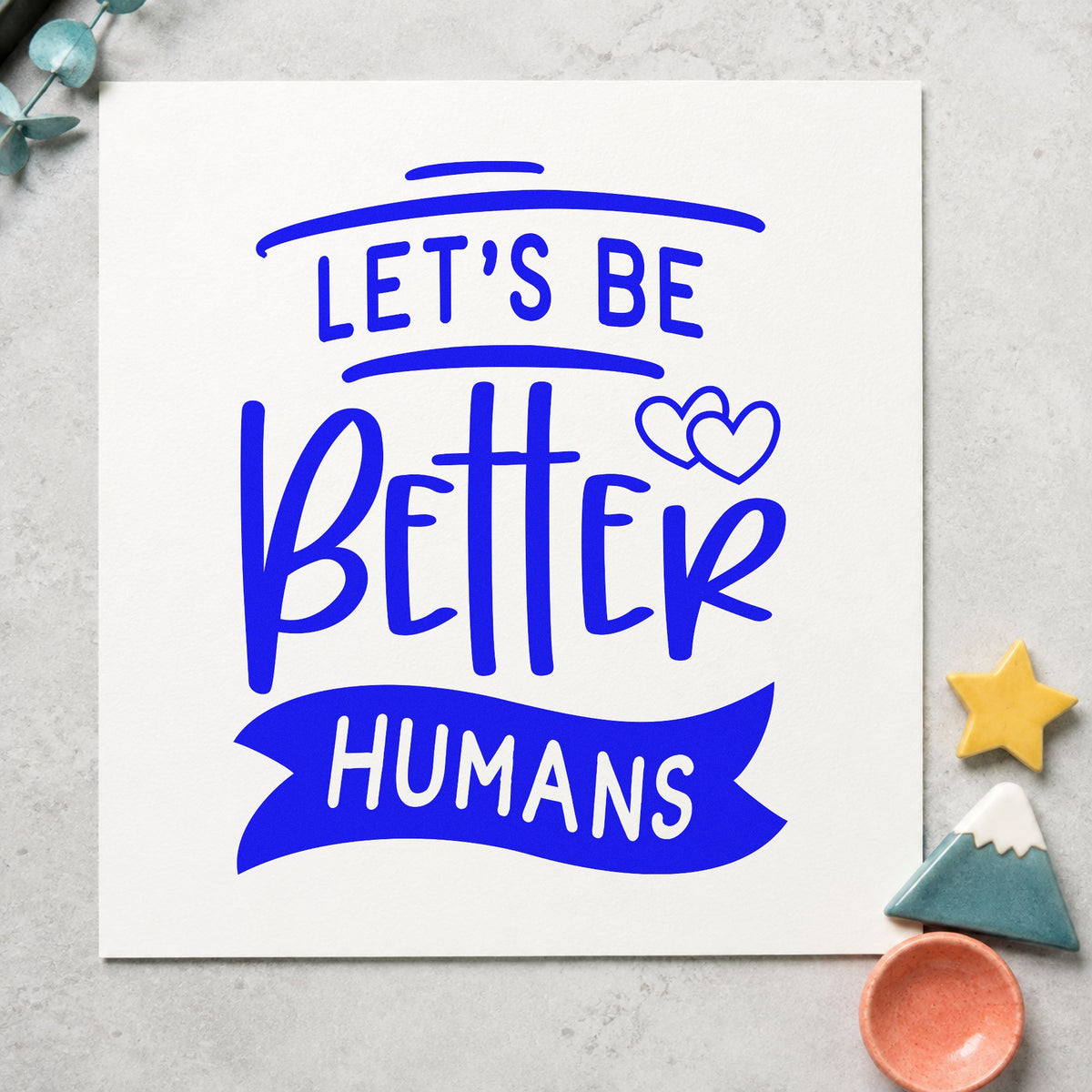 Let's Be Better Humans craft stamp in blue ink on cardstock, an easy option for chair throw printing.