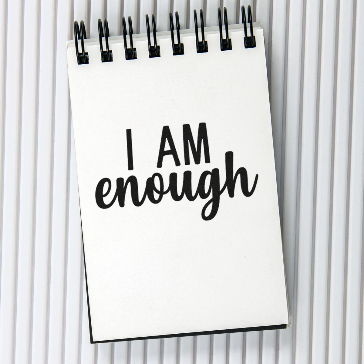 White spiral notepad stamp with black I AM enough on a light gray seal product background.