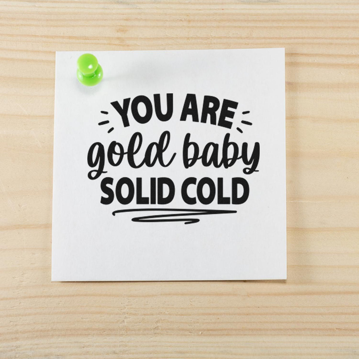 Black stamp/seal design reading You are gold baby solid cold on white paper, with a green pushpin on light wood.