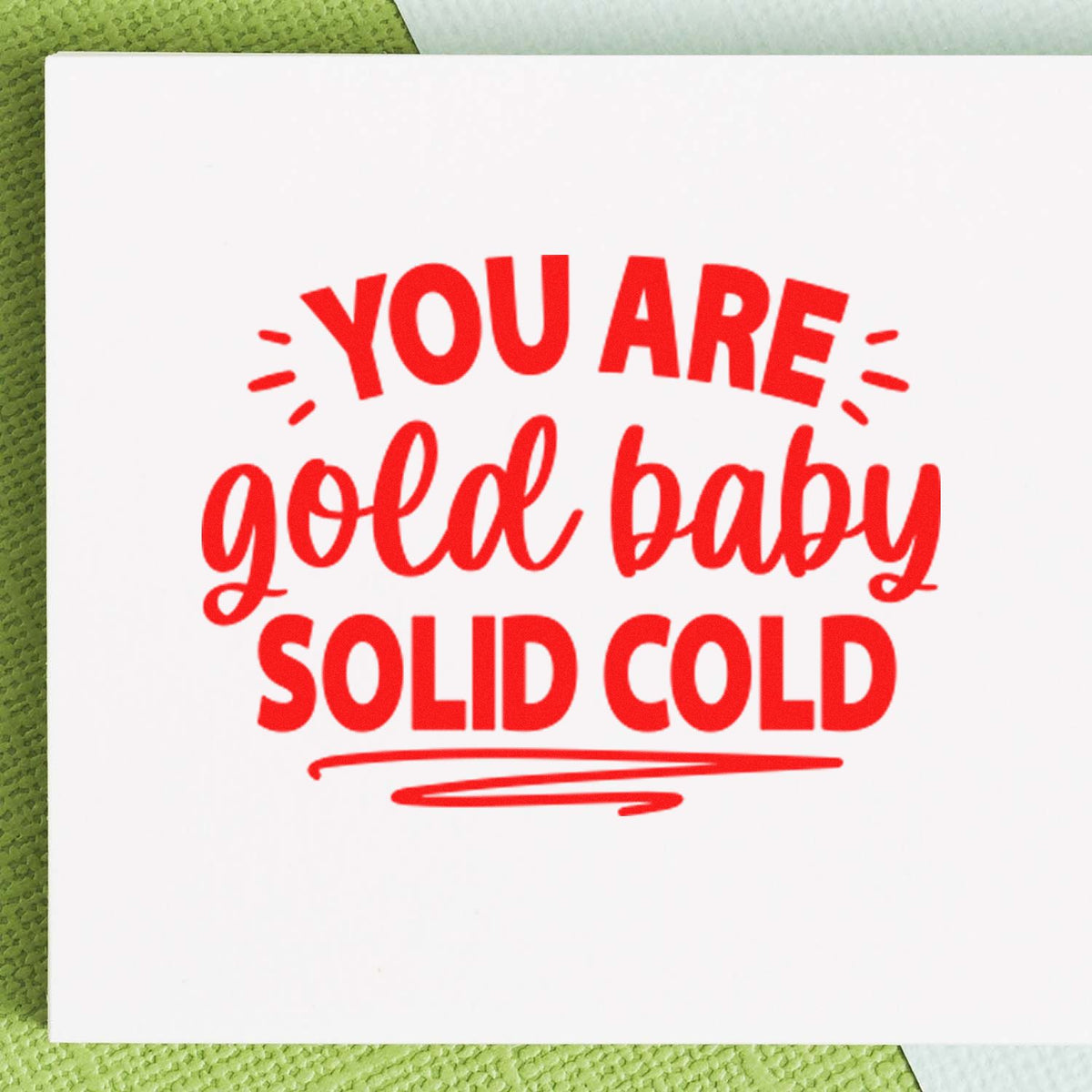 Red stamp-style seal reading YOU ARE gold baby SOLID COLD on white card with green textured background.