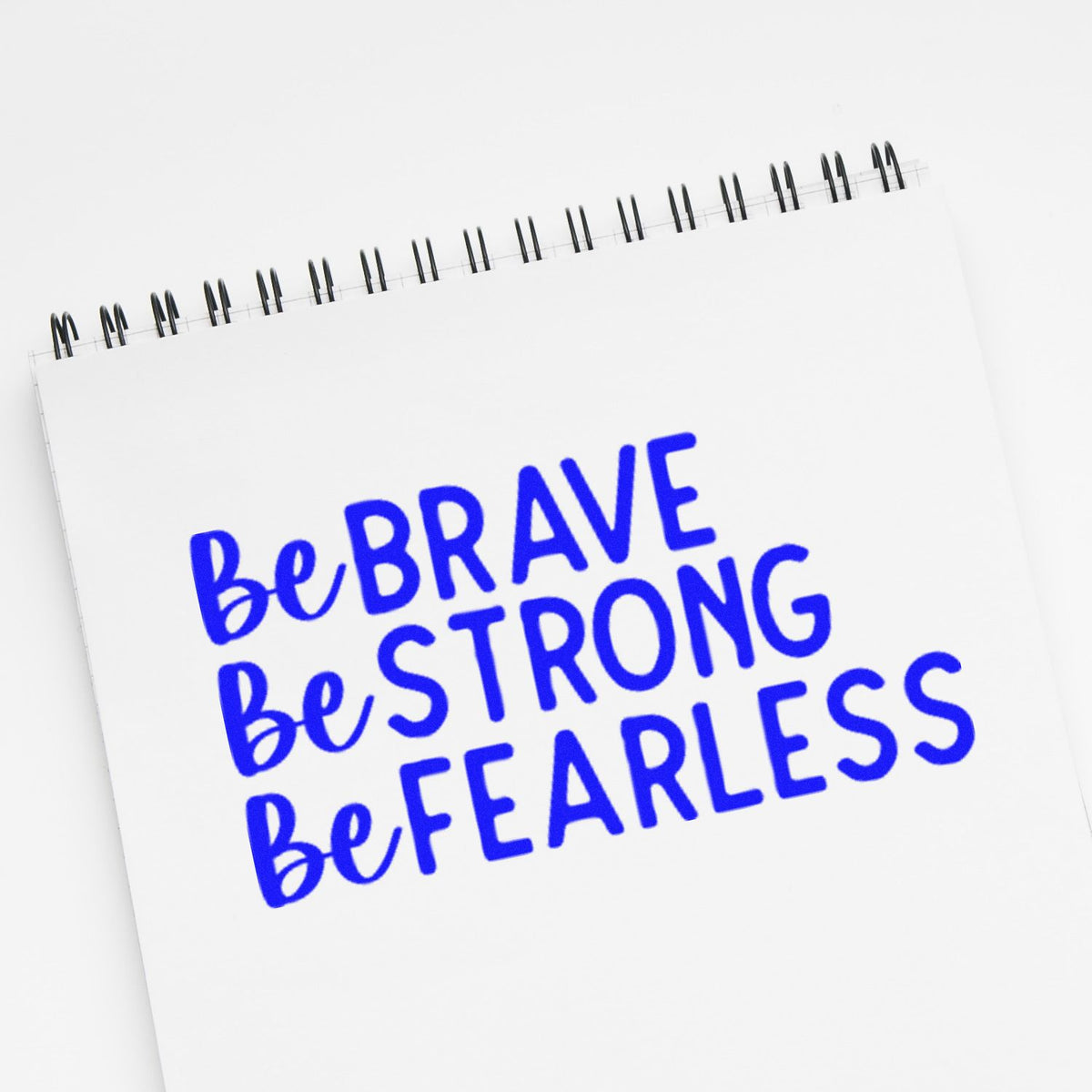 Blue stamp and seal on white spiral notepad reading Be Brave Be Strong Be Fearless.