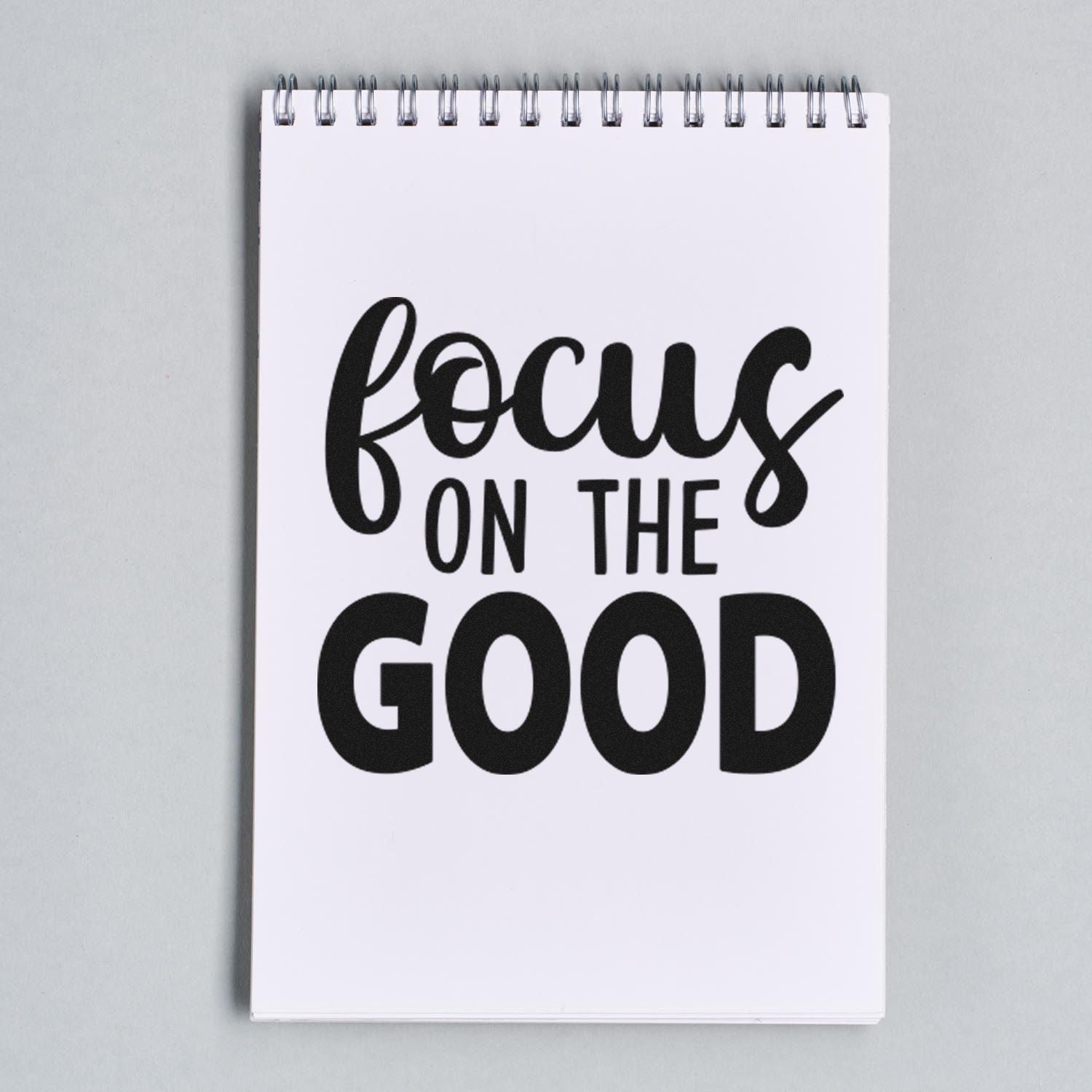 Black Focus on the Good stamp and seal design on a white spiral notebook, bold black script and block lettering.