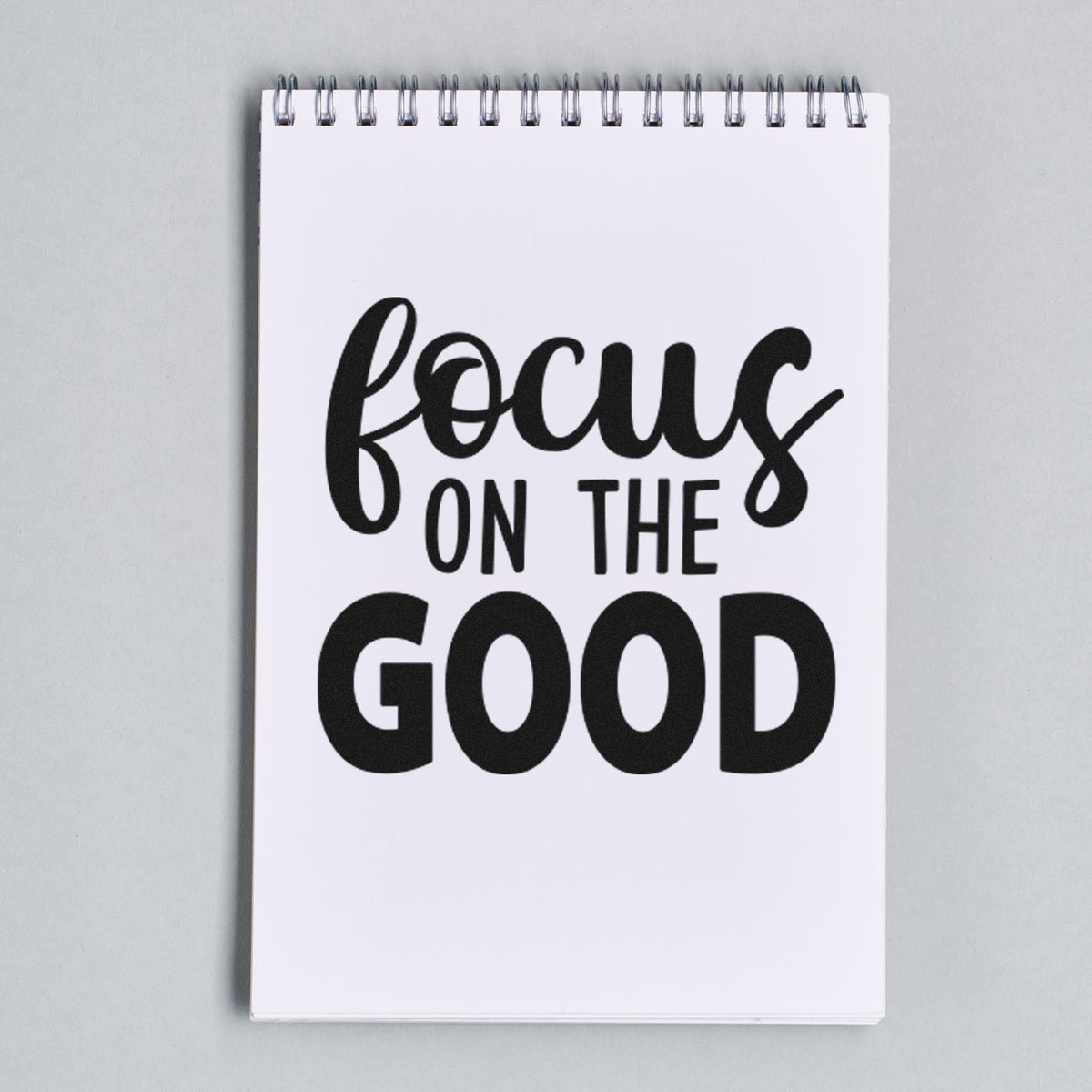 Black stamp and seal design on a white spiral notepad with bold text reading focus on the good.