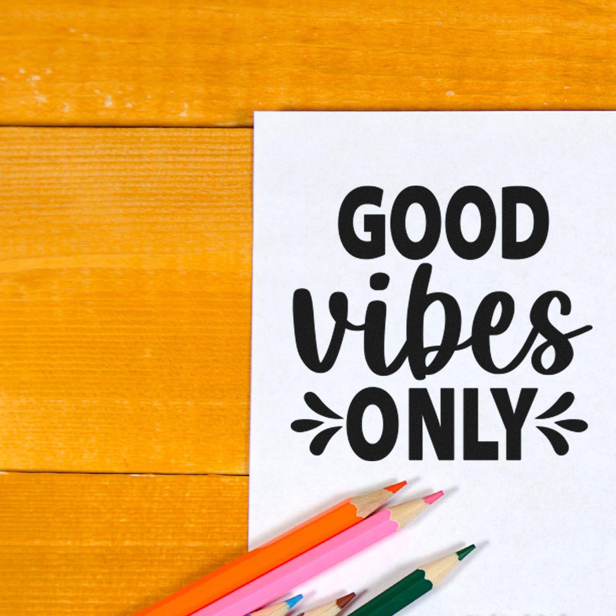 Black Good Vibes Only stamp seal on white paper, with orange wood background and colored pencils