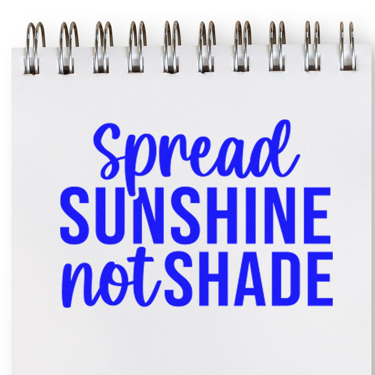 Blue spiral-bound notebook with a stamped Spread Sunshine Not Shade design in bold blue script and block letters.