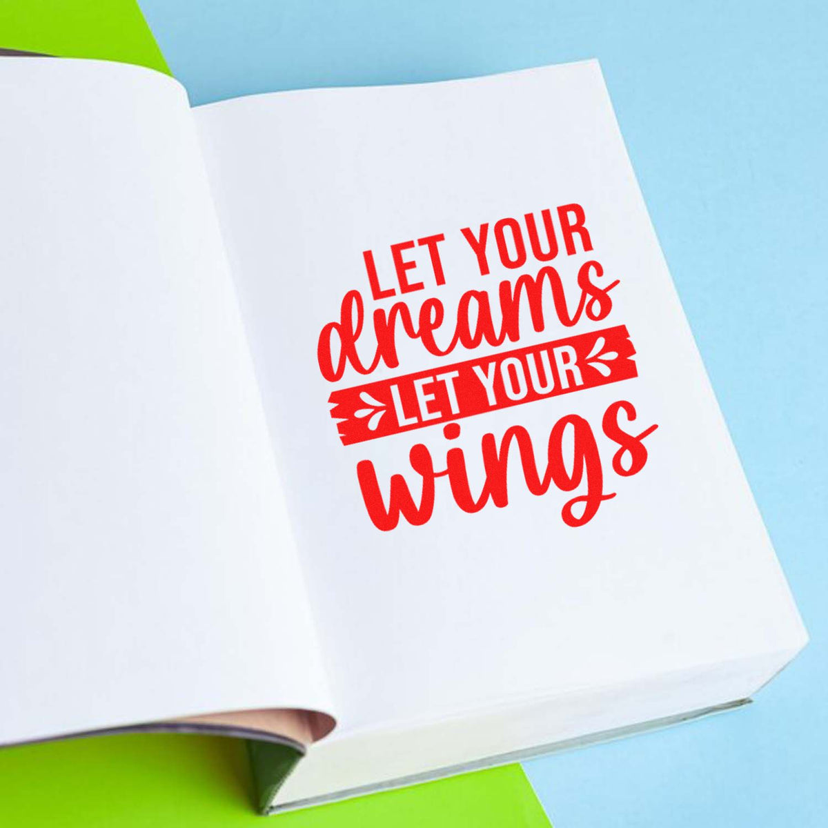 Red stamp/seal text Let Your Dreams Let Your Wings on a white notebook page with blue background and green accents.