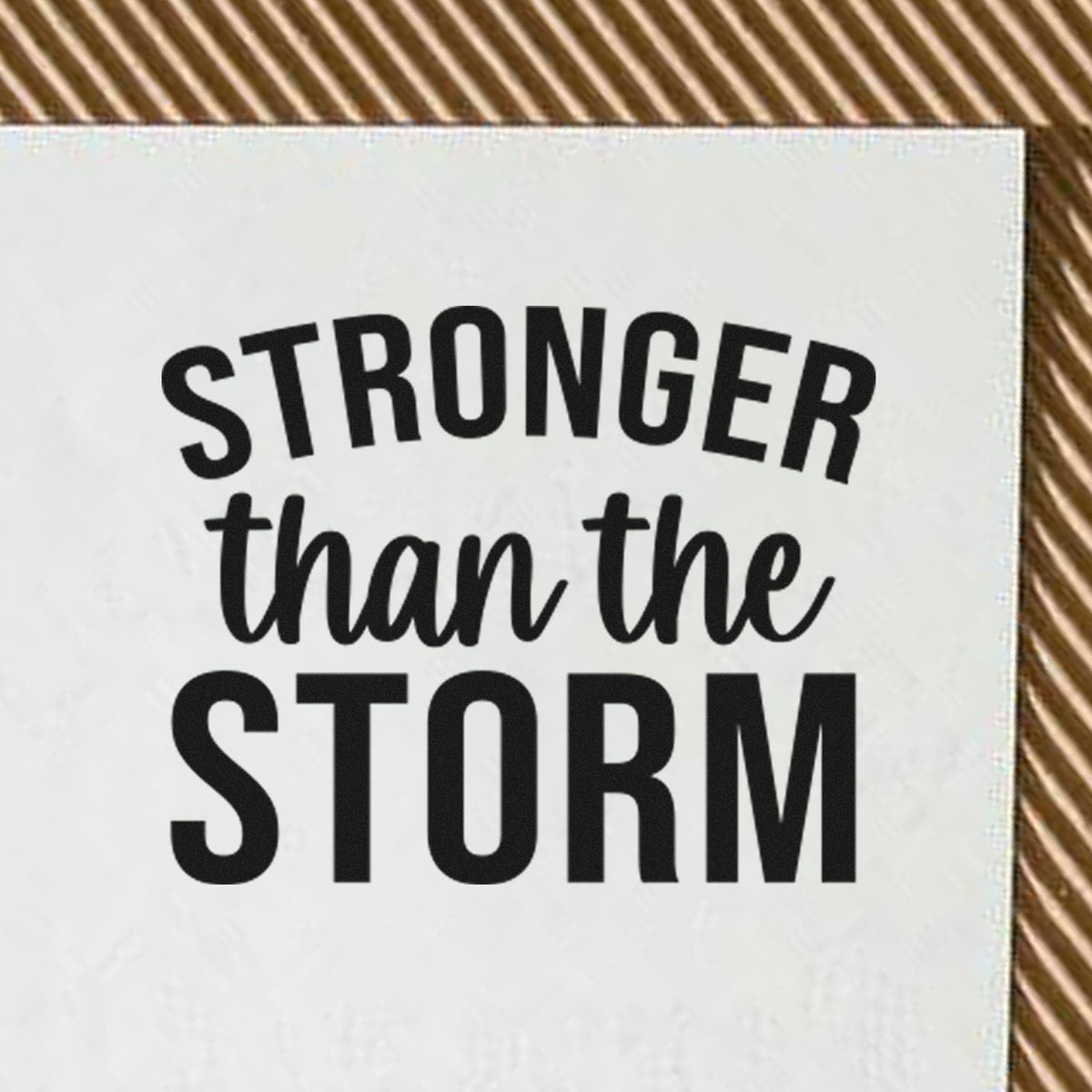 White stamp seal with bold black STRONGER than the STORM text on a brown striped background.