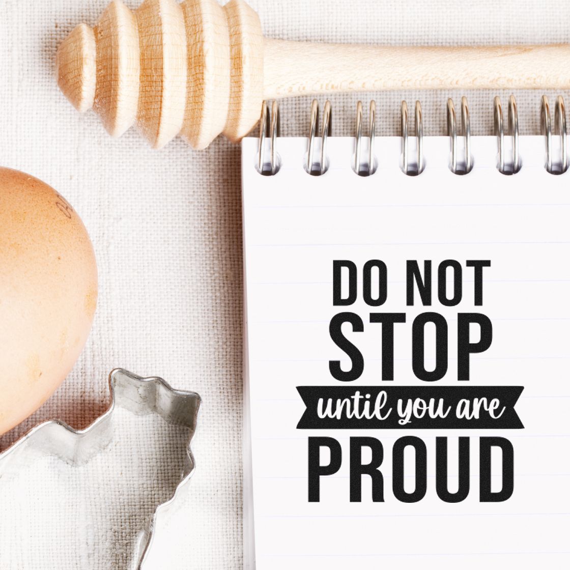 Black Do Not Stop Until You Are Proud stamp and seal on white spiral notebook, with wooden handle and beige cloth.