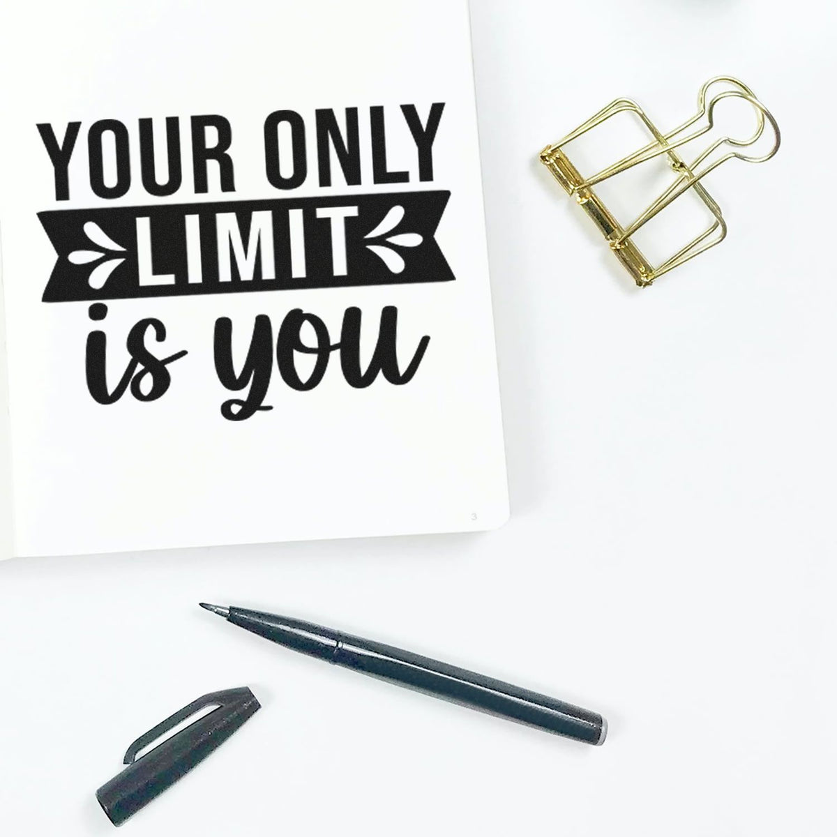 Black custom stamp-and-seal design on white paper with gold binder clip, black pen, and cap on a white background.