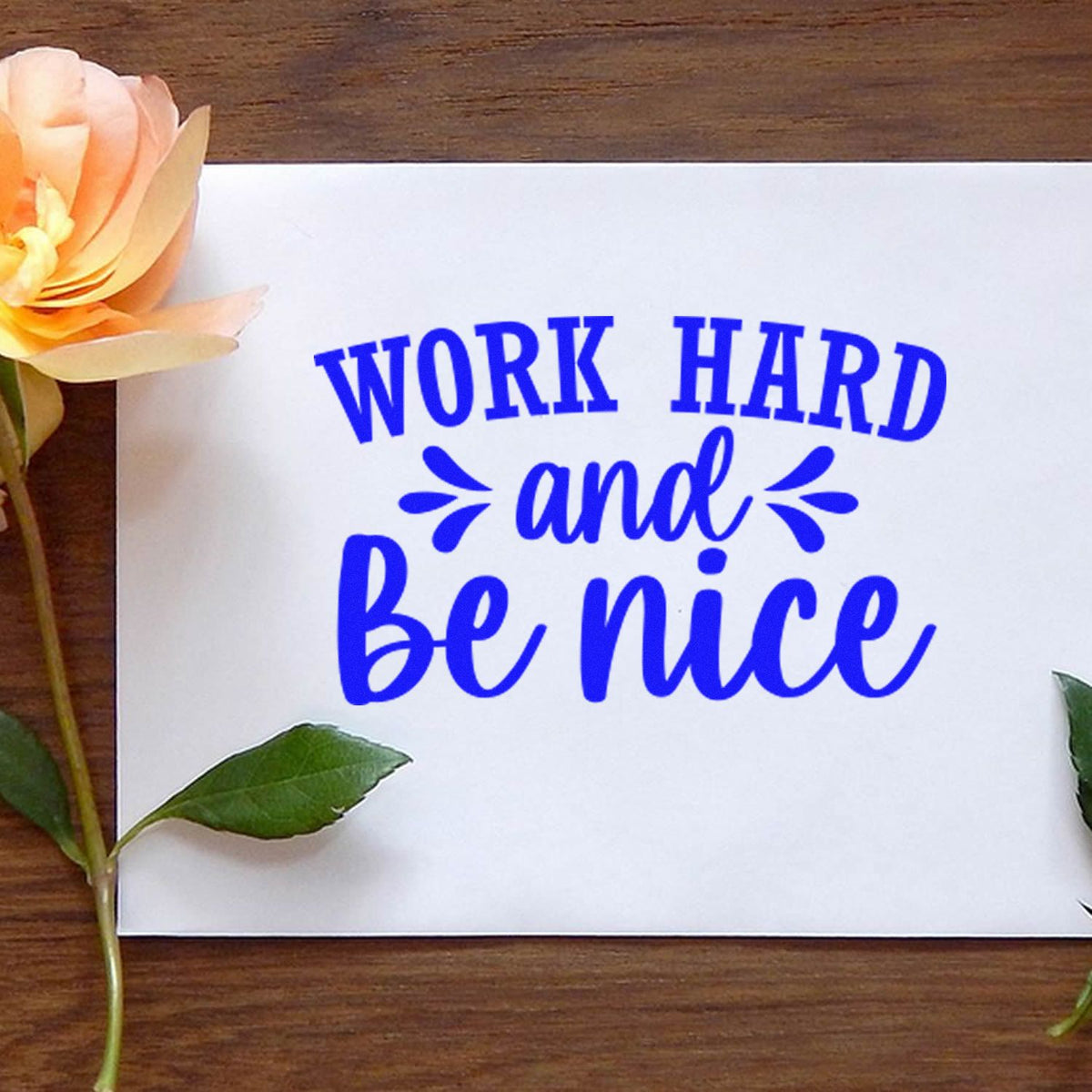 Blue stamp/seal design with Work hard and be nice on white paper, accented by a peach flower and green leaves.
