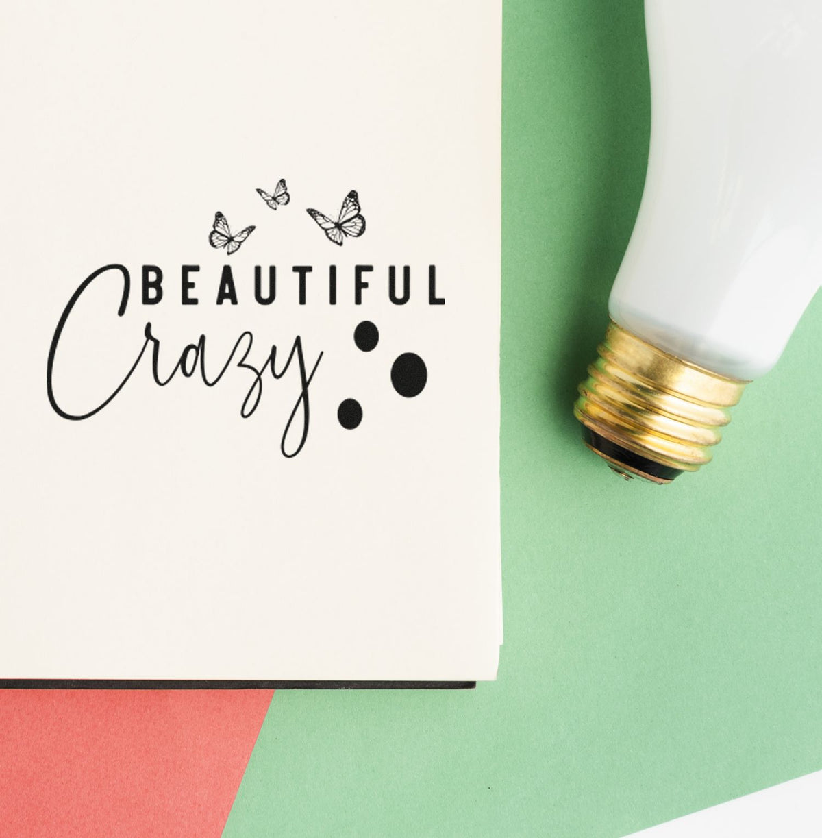 Black butterfly stamp reading Beautiful Crazy beside a white-and-gold seal tool on green background.