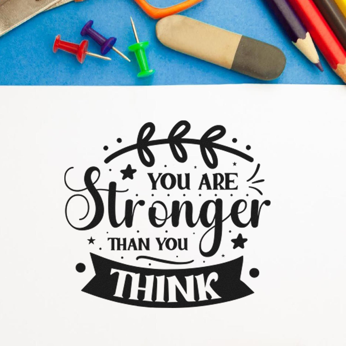 Black motivational rubber stamp reading You are stronger than you think with colorful push pins on blue background.
