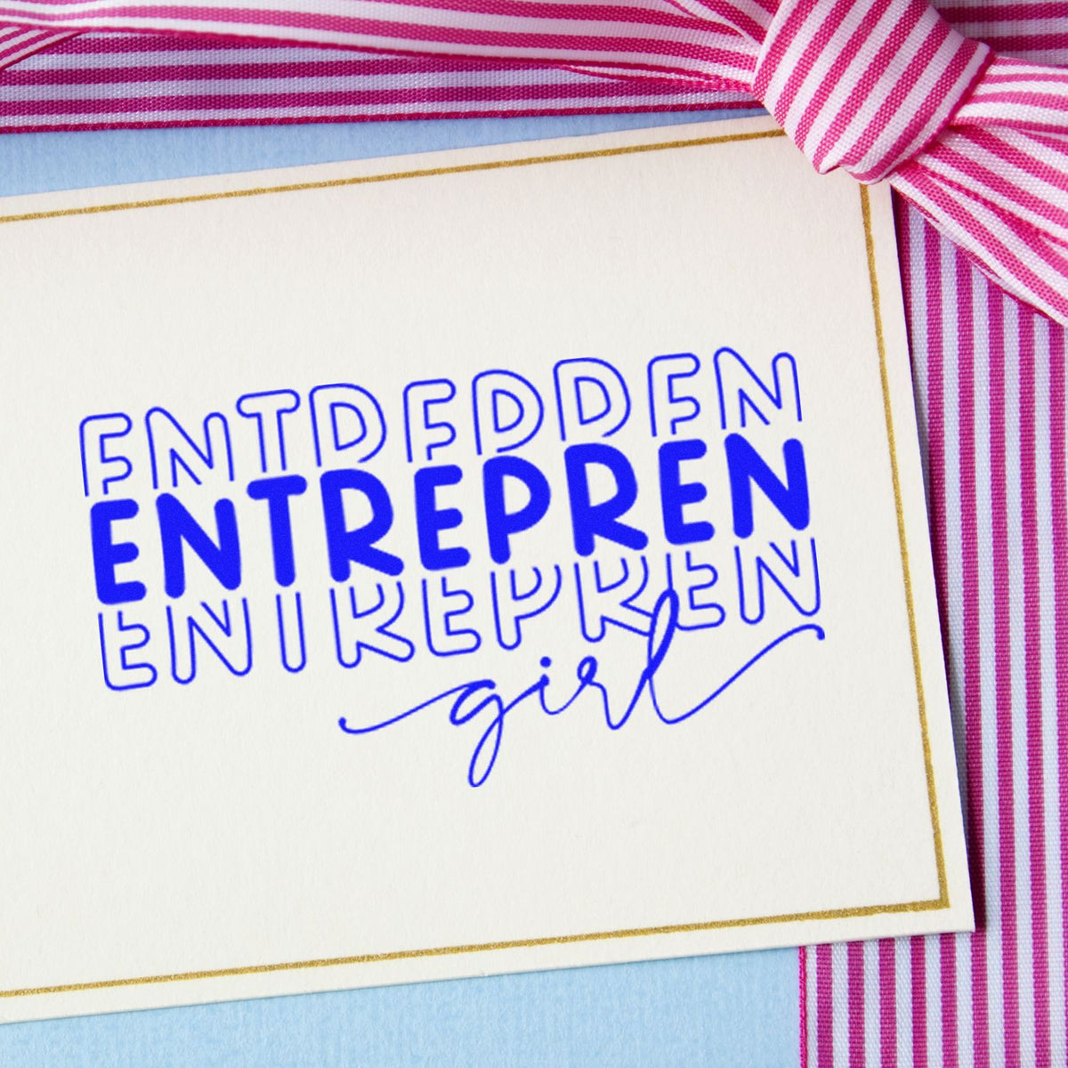 Blue entrepreneur girl stamp and seal on white card with gold border, beside a pink striped ribbon.
