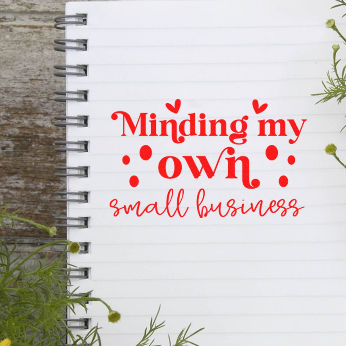 Red stamp and seal reading Minding my own small business on a white spiral notebook with heart accents.