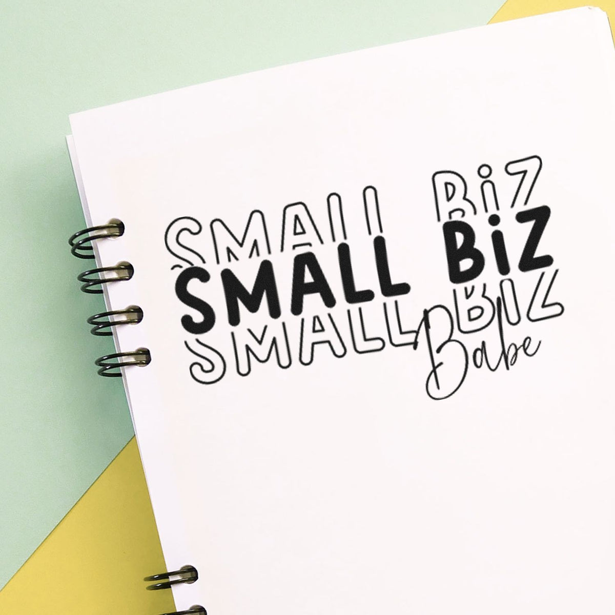 Black stamp and seal designs reading SMALL and BiZ on white spiral-bound pages, with mint green and yellow background.