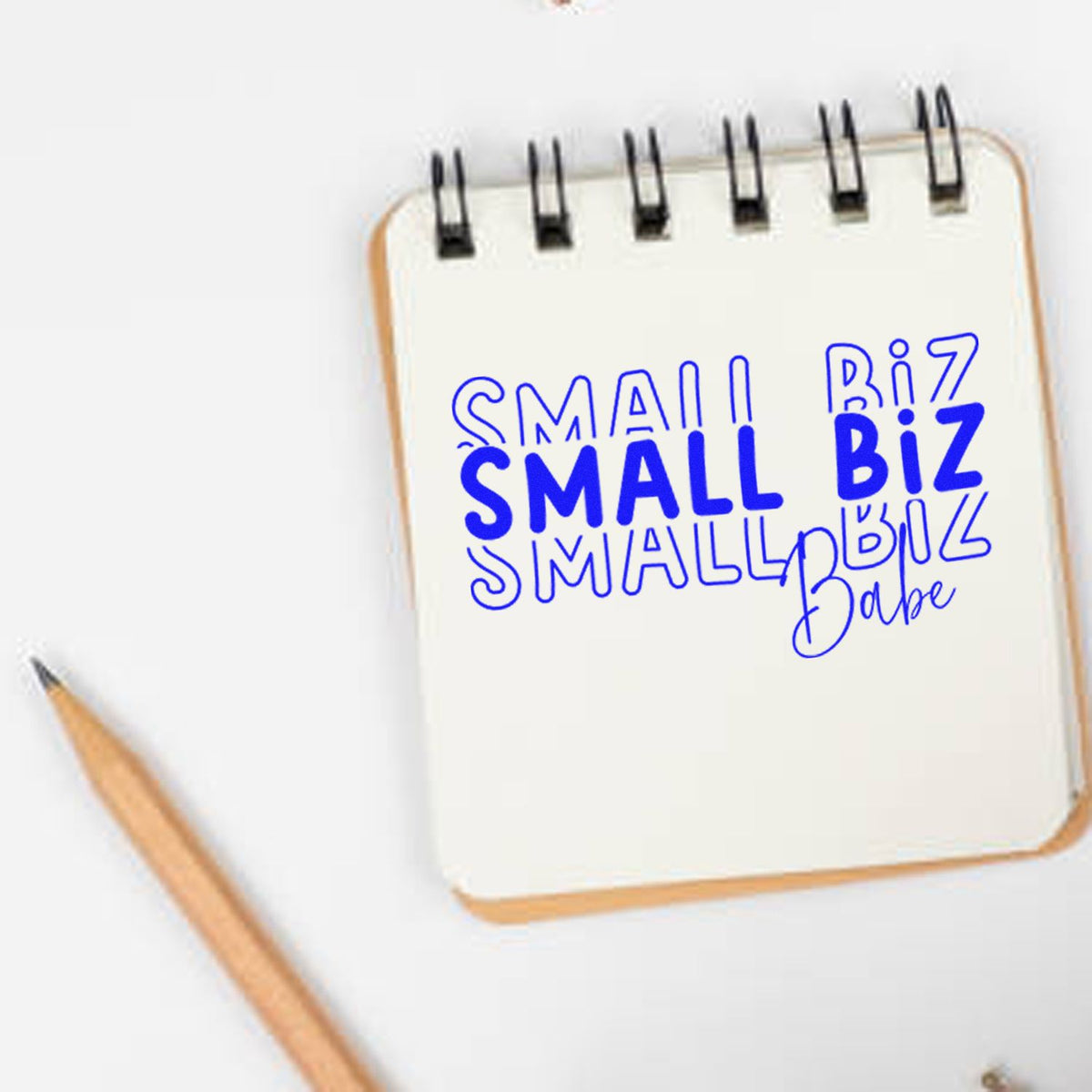 Custom stamp and seal design on a white spiral notebook, featuring bold blue Small Biz lettering and a wooden pencil.