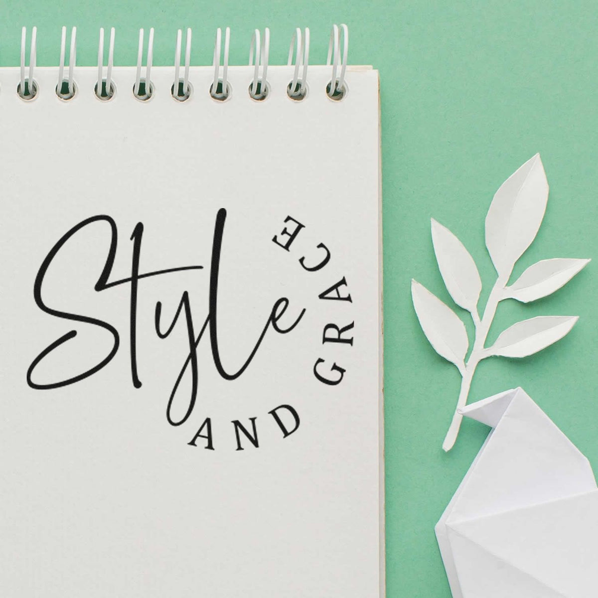 White spiral notebook with black Style and Grace stamp and white paper leaf seal on mint green background.