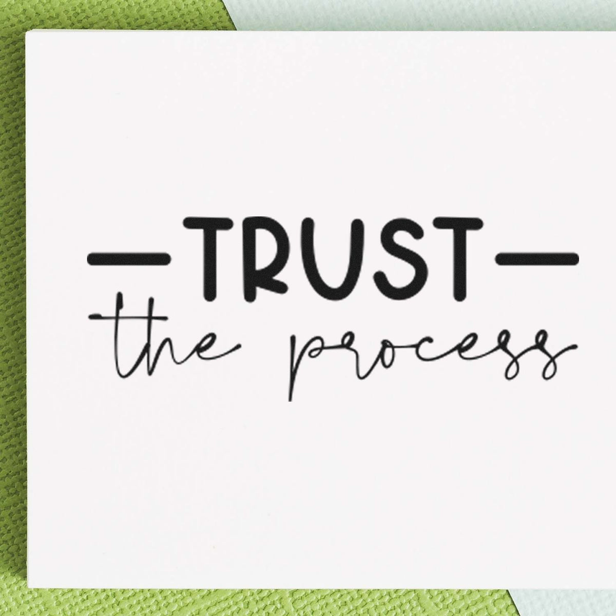 Black TRUST the process stamp seal on a white card over a green textured background.