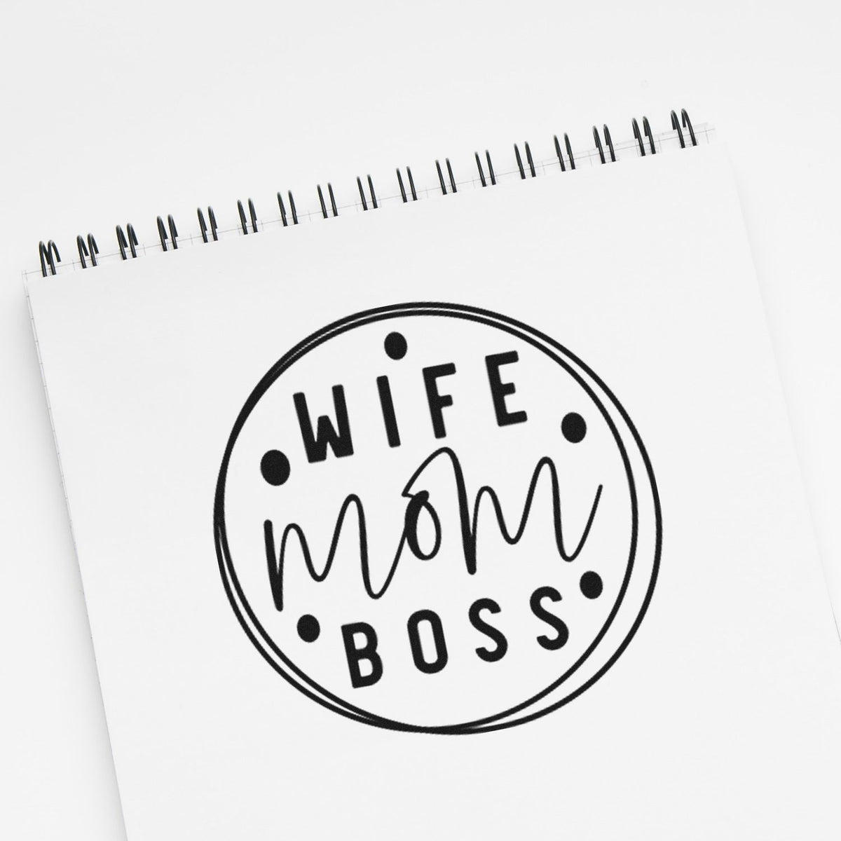 Black circular stamp seal on white spiral notebook, reading WIFE mom BOSS