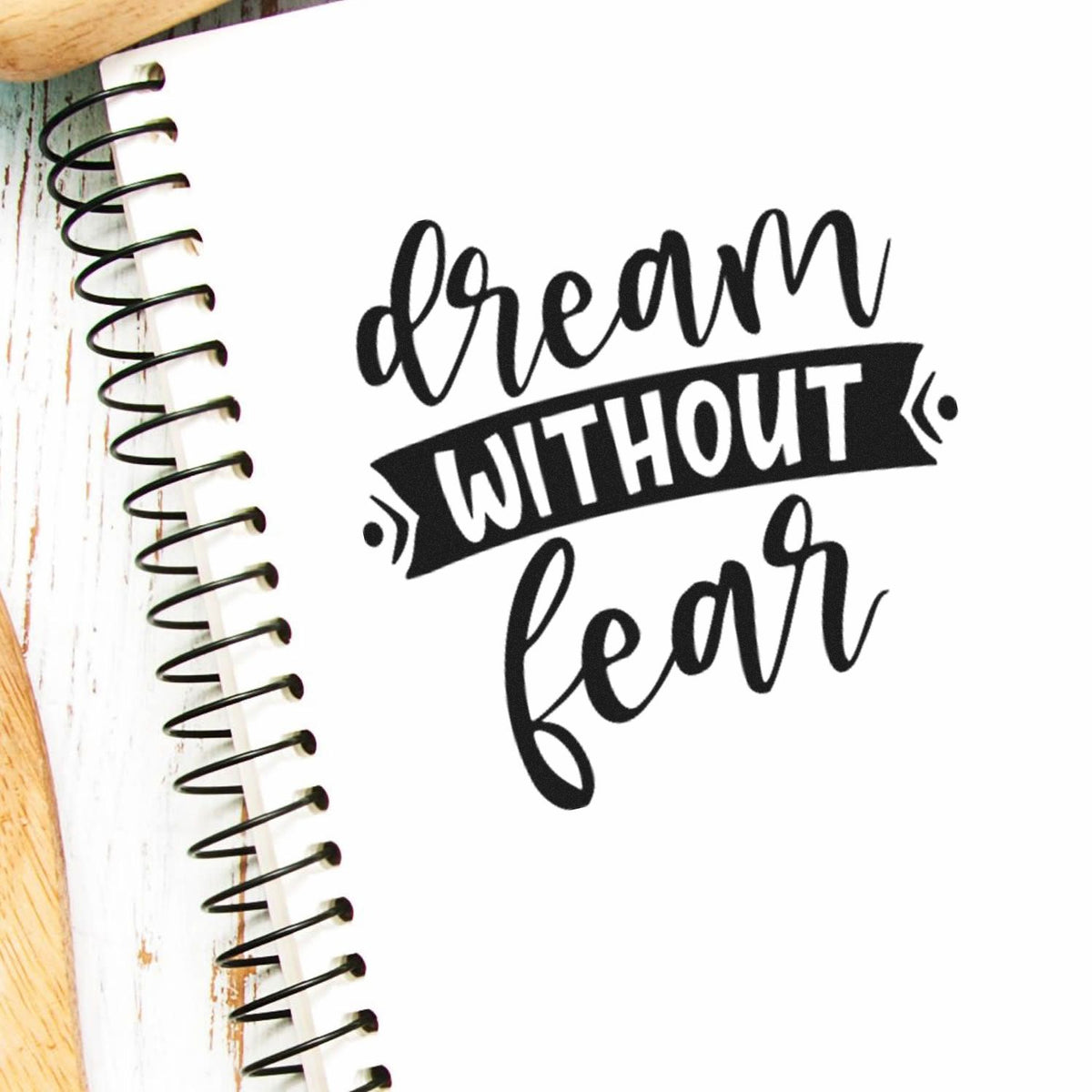 Black dream without fear stamp design on white notebook with spiral binding and wood edges.