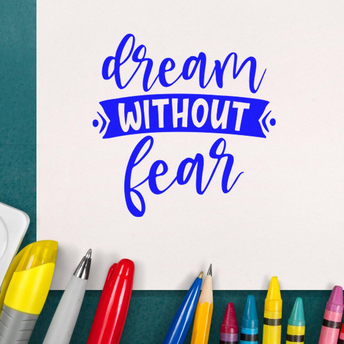 Blue dream without fear stamp seal design on white paper, surrounded by colorful pens and markers.