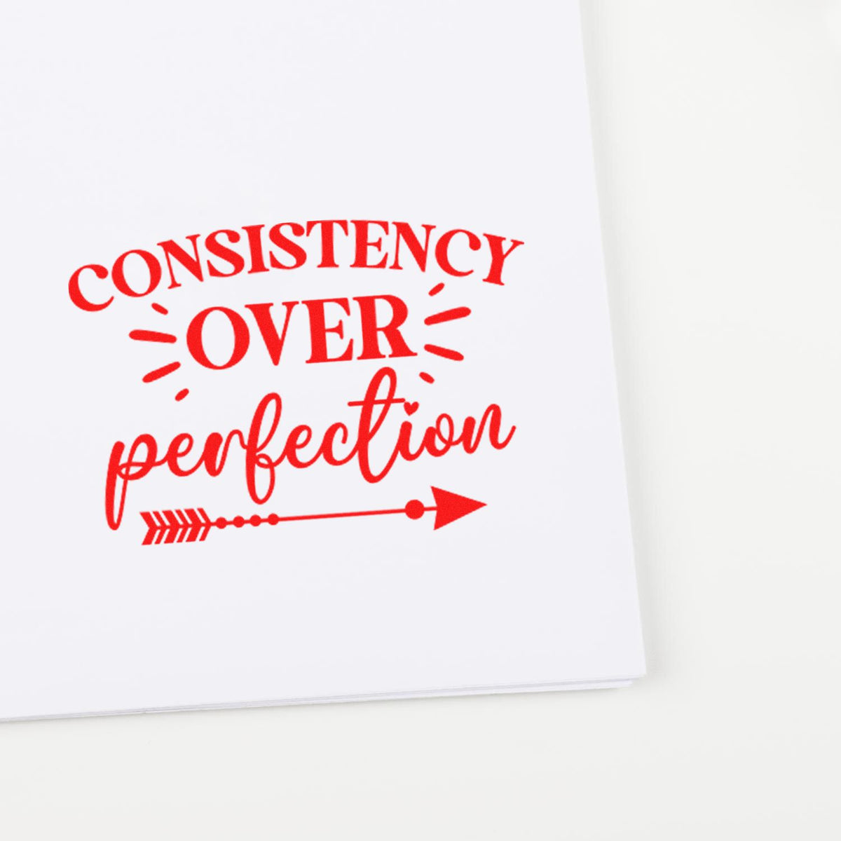 Red self-inking stamp on white paper reading Consistency over perfection with arrow graphic.