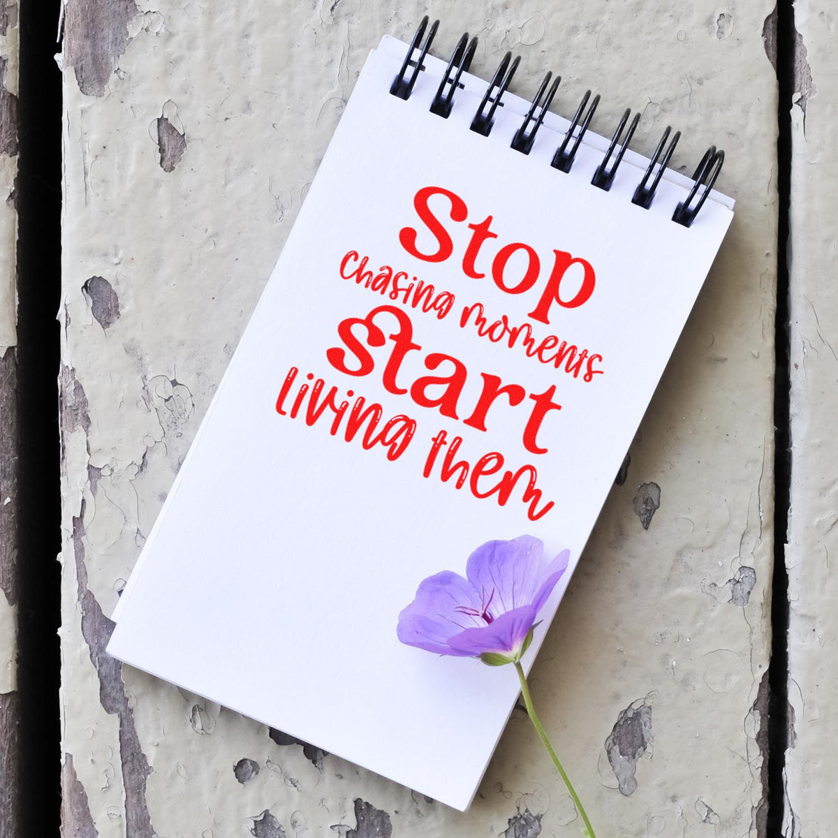 Red stamp-style seal on white spiral notepad with purple flower on distressed gray background.