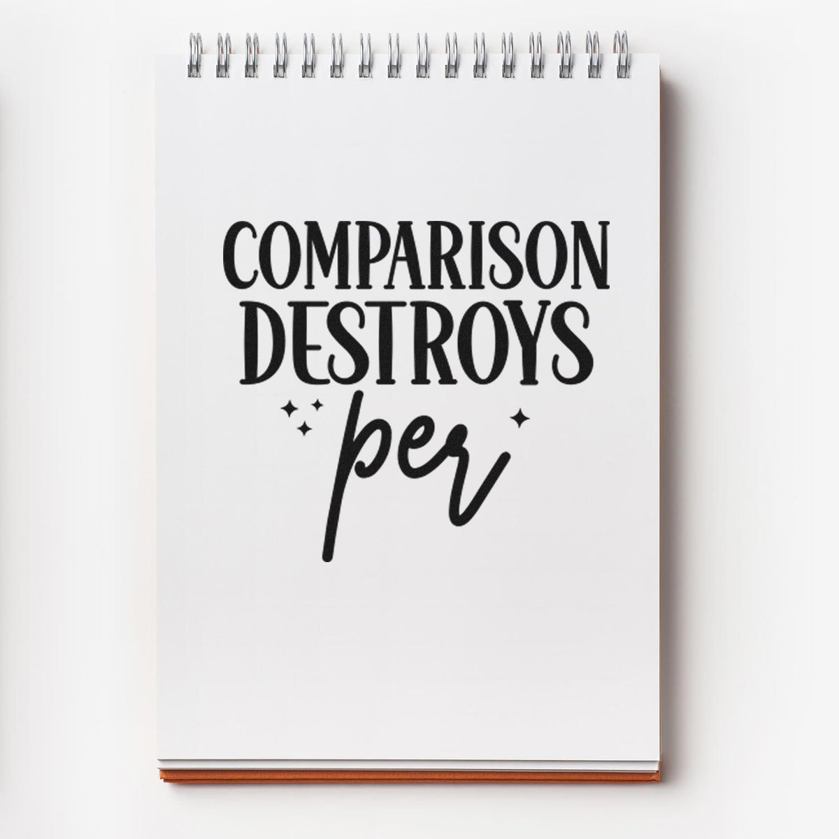 Black stamp and seal design on a white spiral notebook with silver coil binding and bold text: Comparison Destroys per