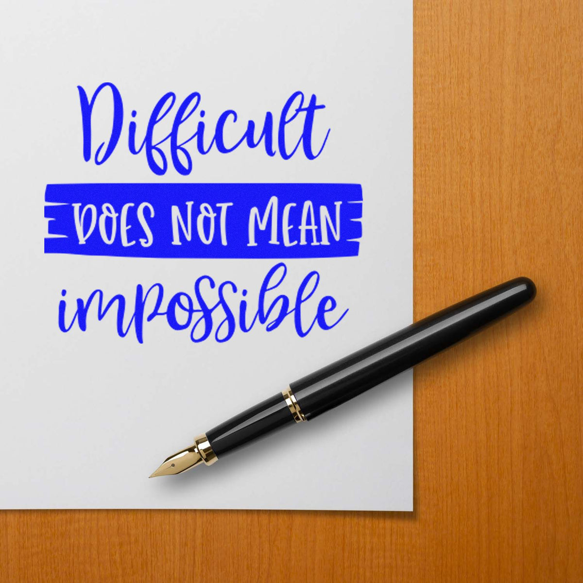 Blue custom stamp and seal text reading Difficult does not mean impossible with black fountain pen on wood desk.