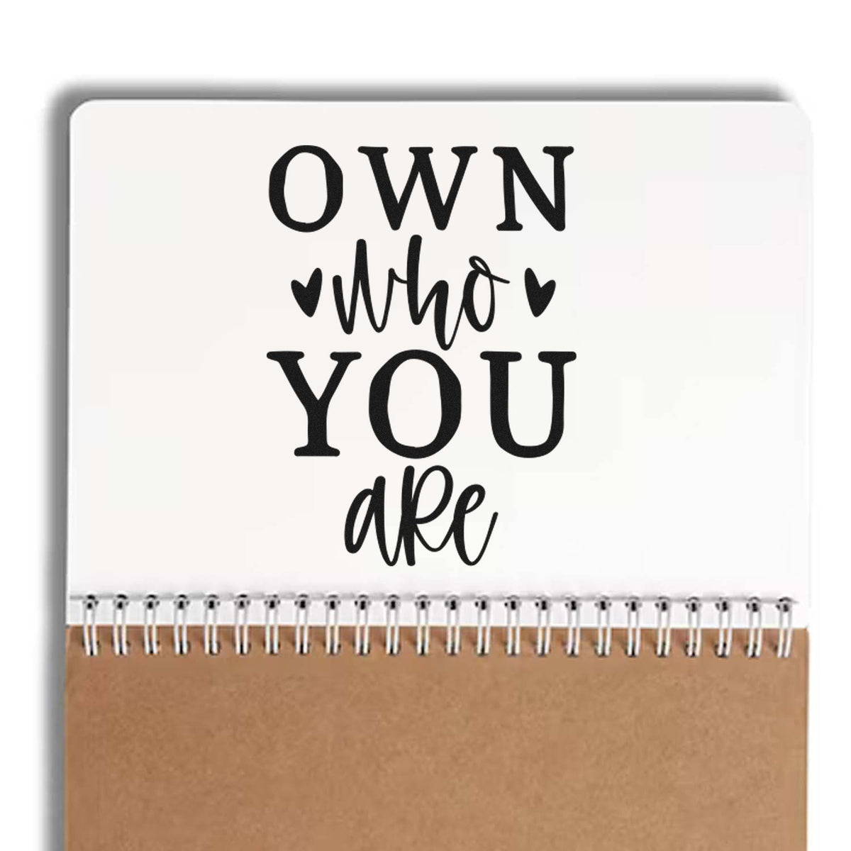 Custom stamp seal notebook cover, white and tan, with black Own who you are lettering and spiral binding.