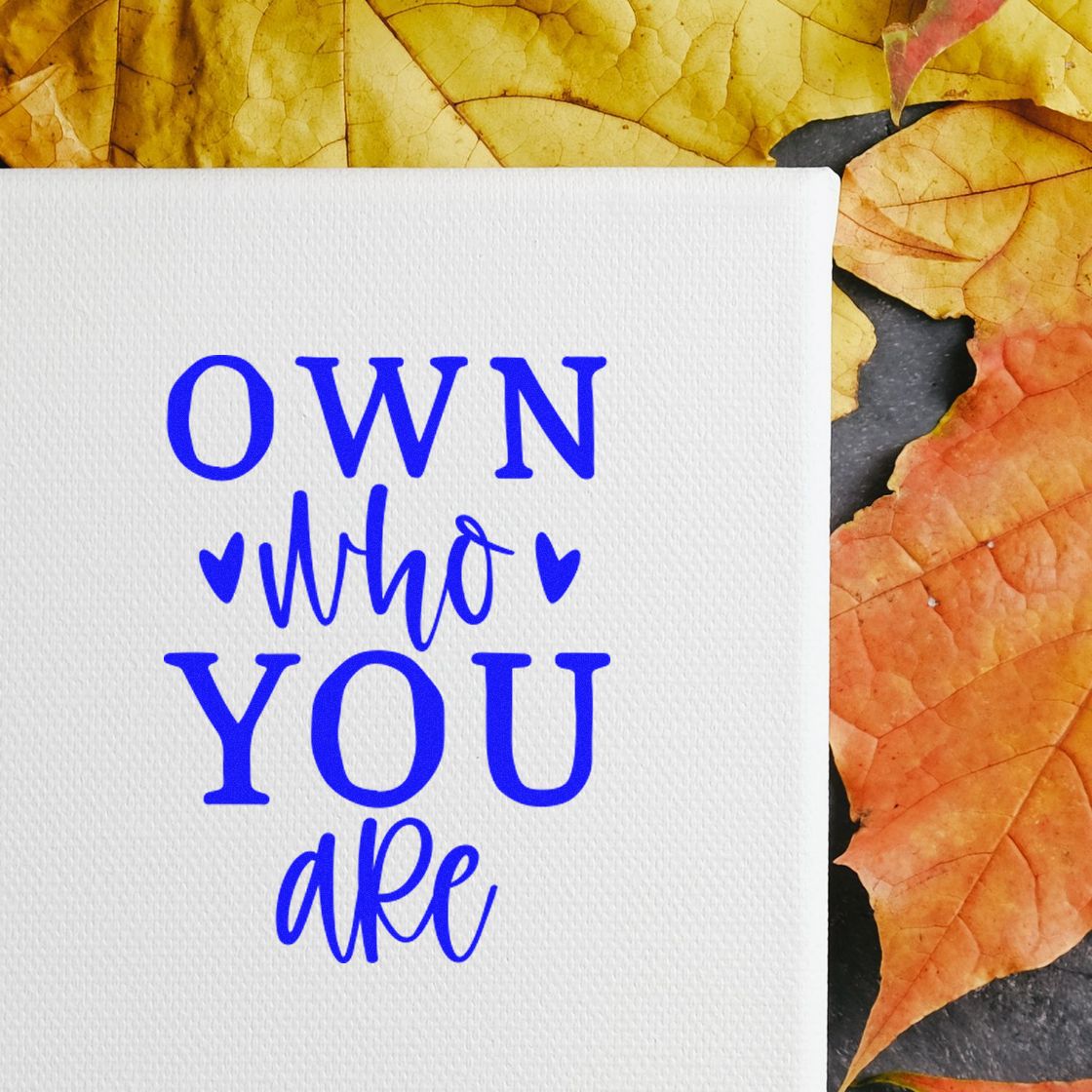 Blue Own who you are stamp on white textured cardstock with hearts, set against orange autumn leaves.