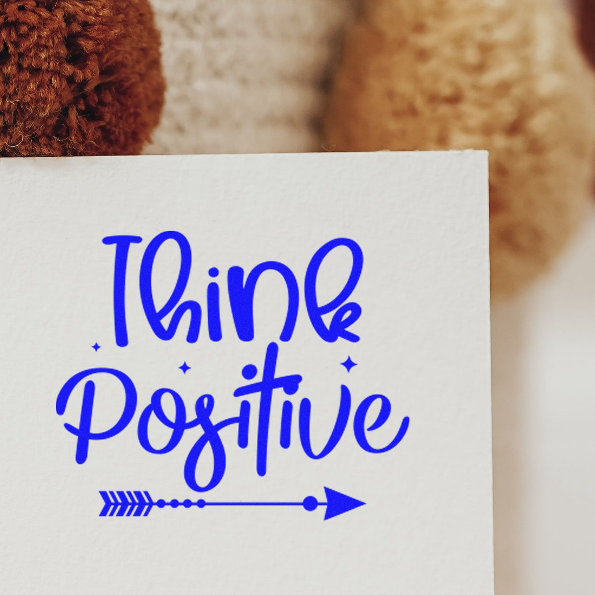 Blue Think Positive stamp seal on white paper, featuring a blue arrow and small star accents.