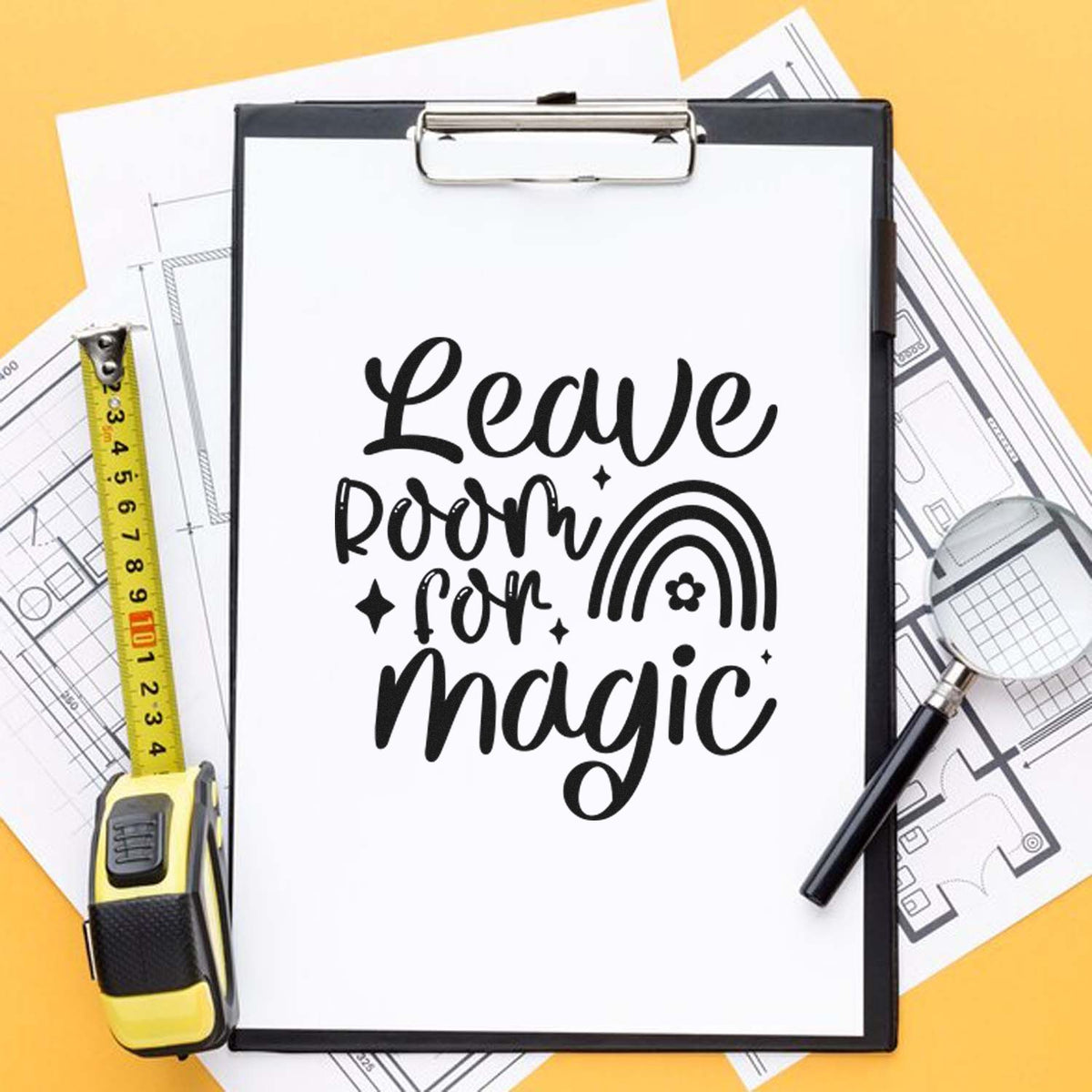 Custom stamp and seal design on white clipboard reading Leave room for magic, with rainbow seal, tape measure, and floor plans on yellow.