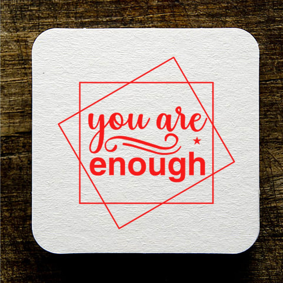 White textured custom stamp seal with red you are enough text and overlapping geometric frames on a dark wood background