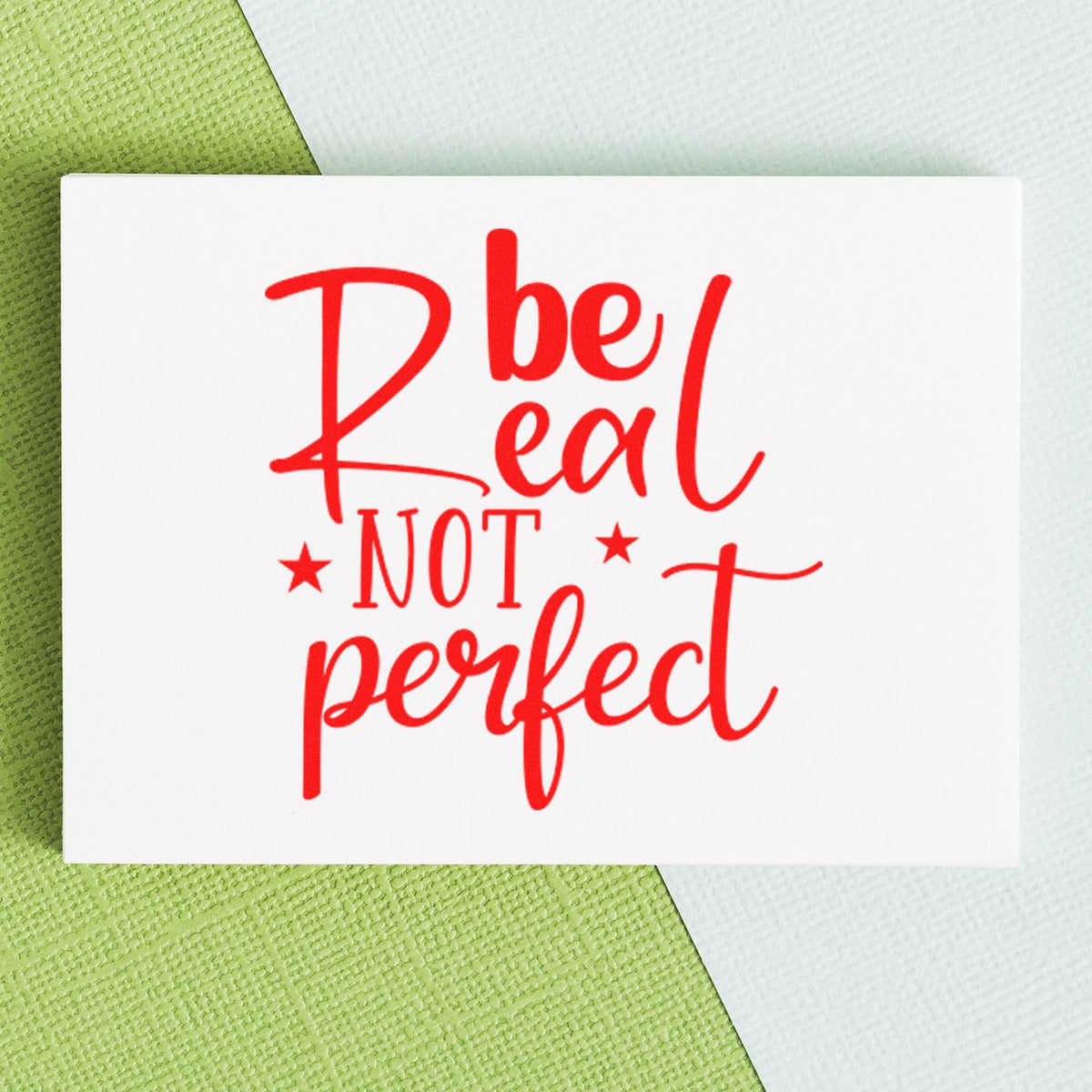 White stamp and seal card with red Be Real Not Perfect lettering on green and white textured background.