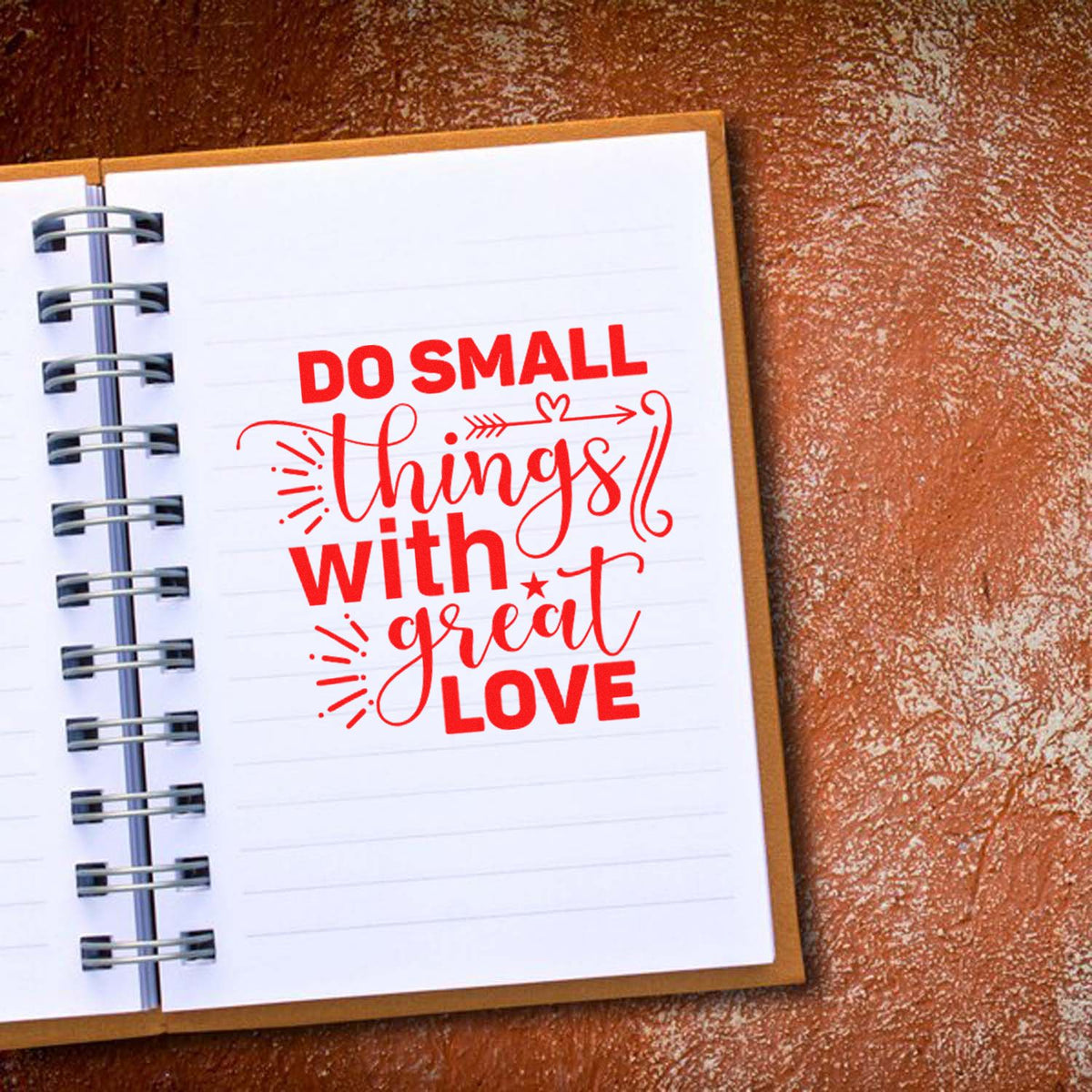 Red stamp-style seal on white spiral notebook page reads Do small things with great love on brown textured background.