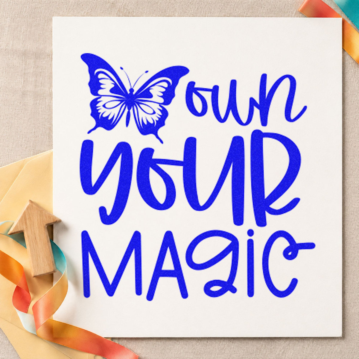 Own Your Magic Butterfly craft stamp imprinted in blue ink on paper, a design suited to framed booth board.