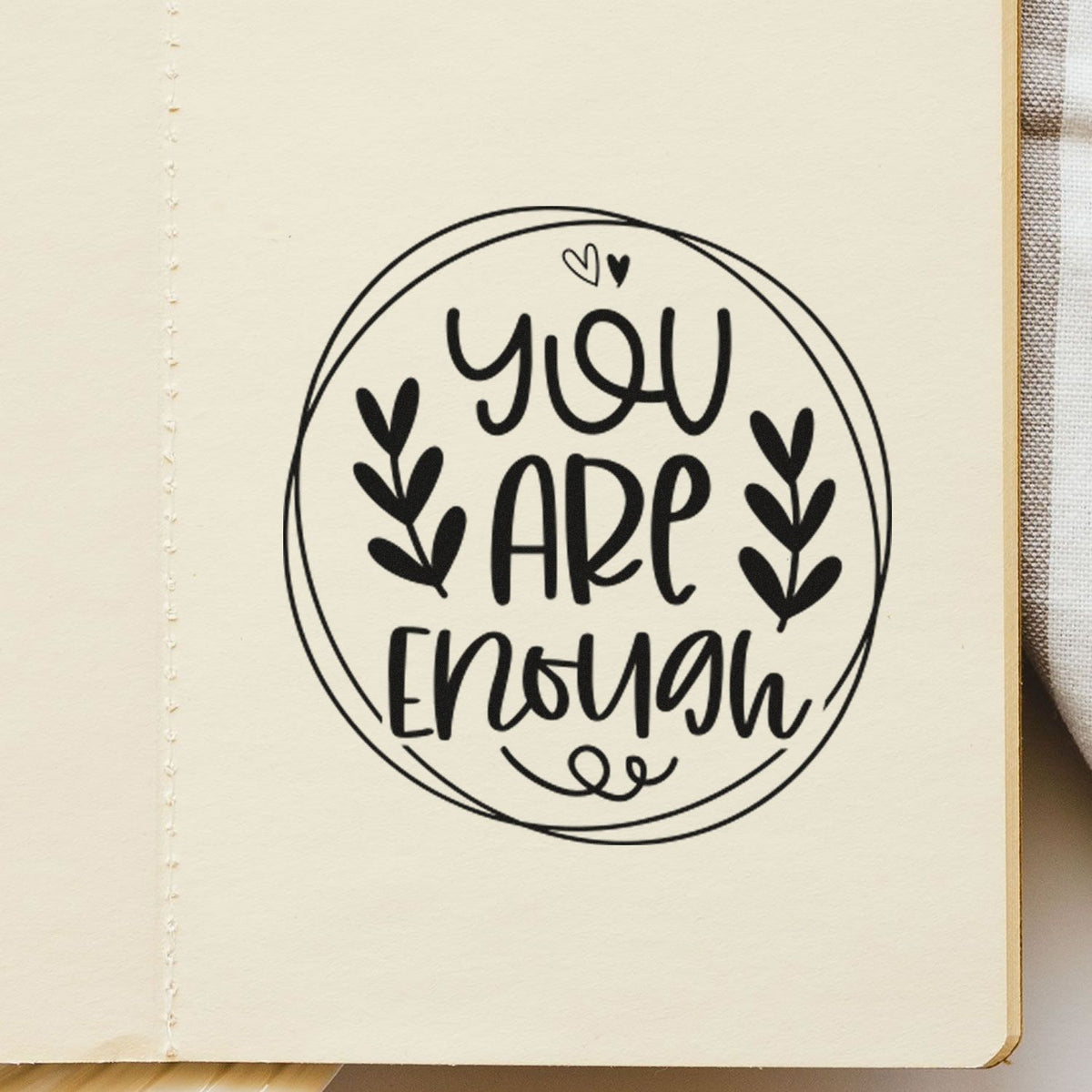 Black circular stamp seal on cream paper reading You are enough with heart leaves and small hearts.