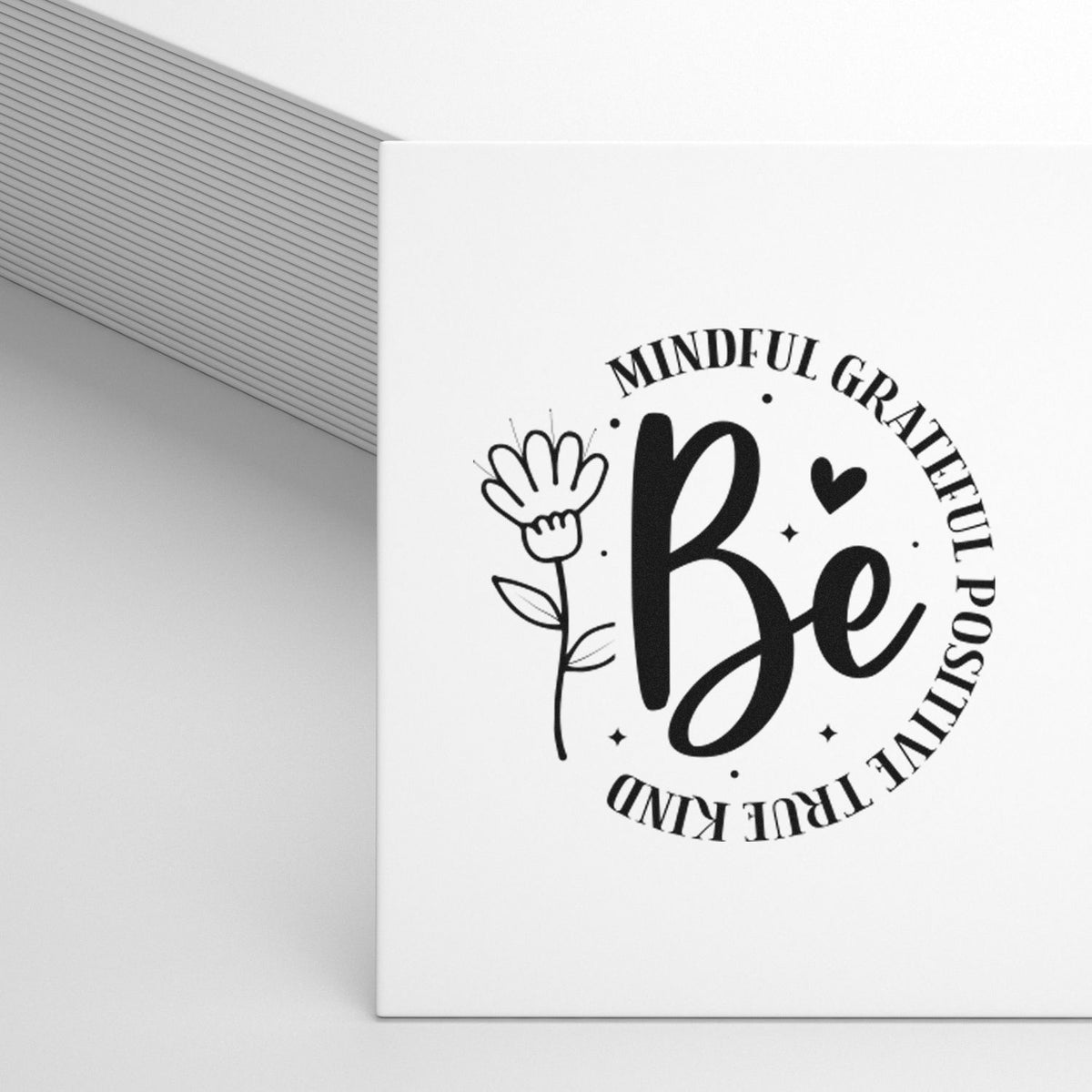 White stamp seal with black Be design, floral line art, and circular text reading Mindful Grateful Positive True Kind.