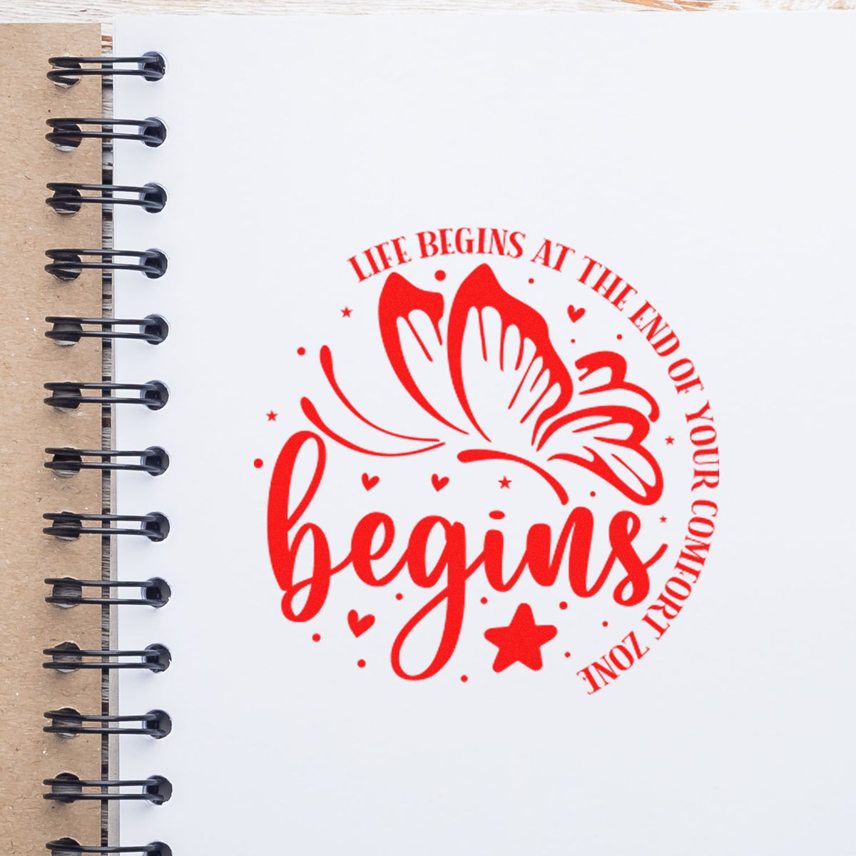 Red butterfly stamp and seal design with begins text, hearts and stars on a white spiral notebook.