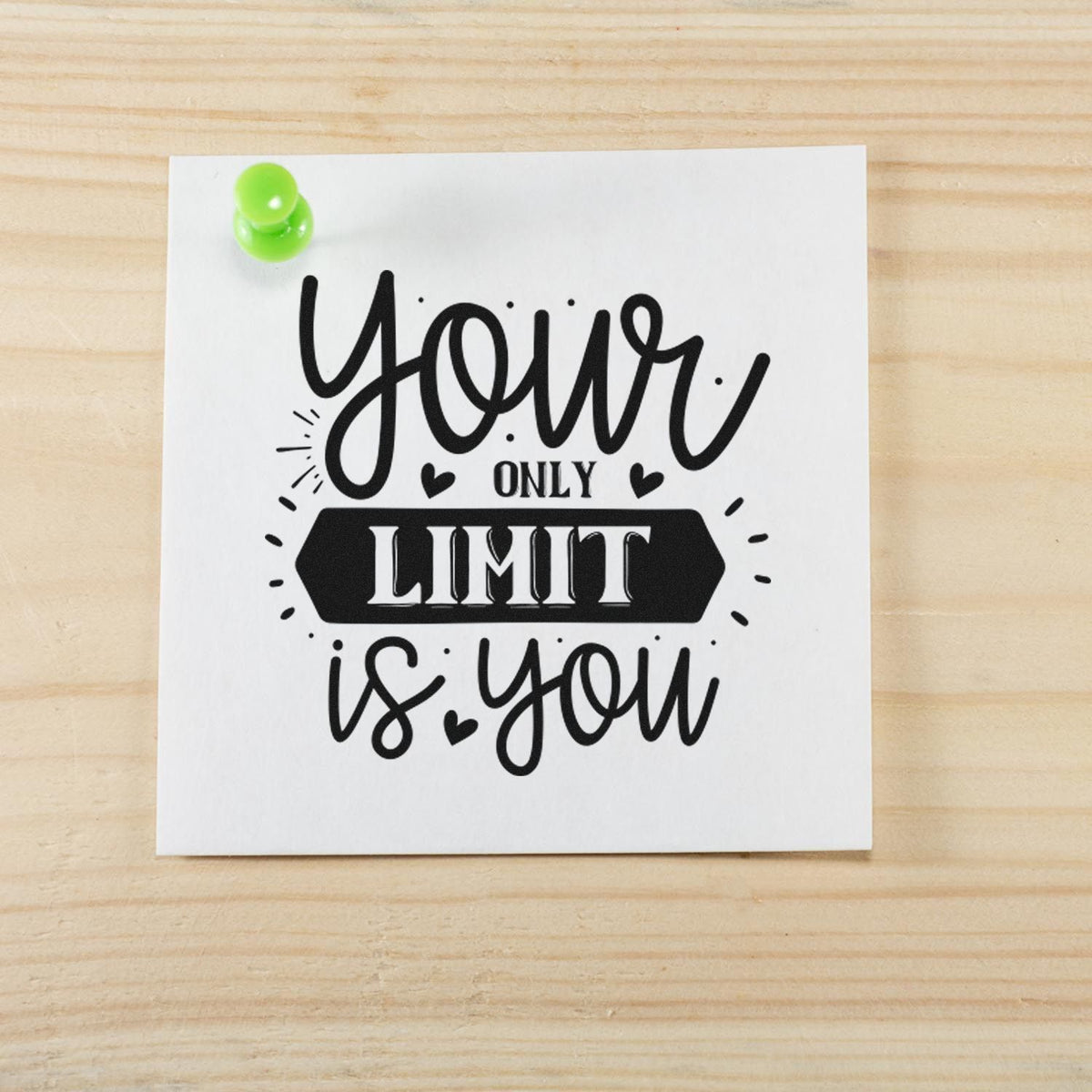 Black custom stamp imprint on white paper with green push pin, reading your only limit is you on a light wood background.